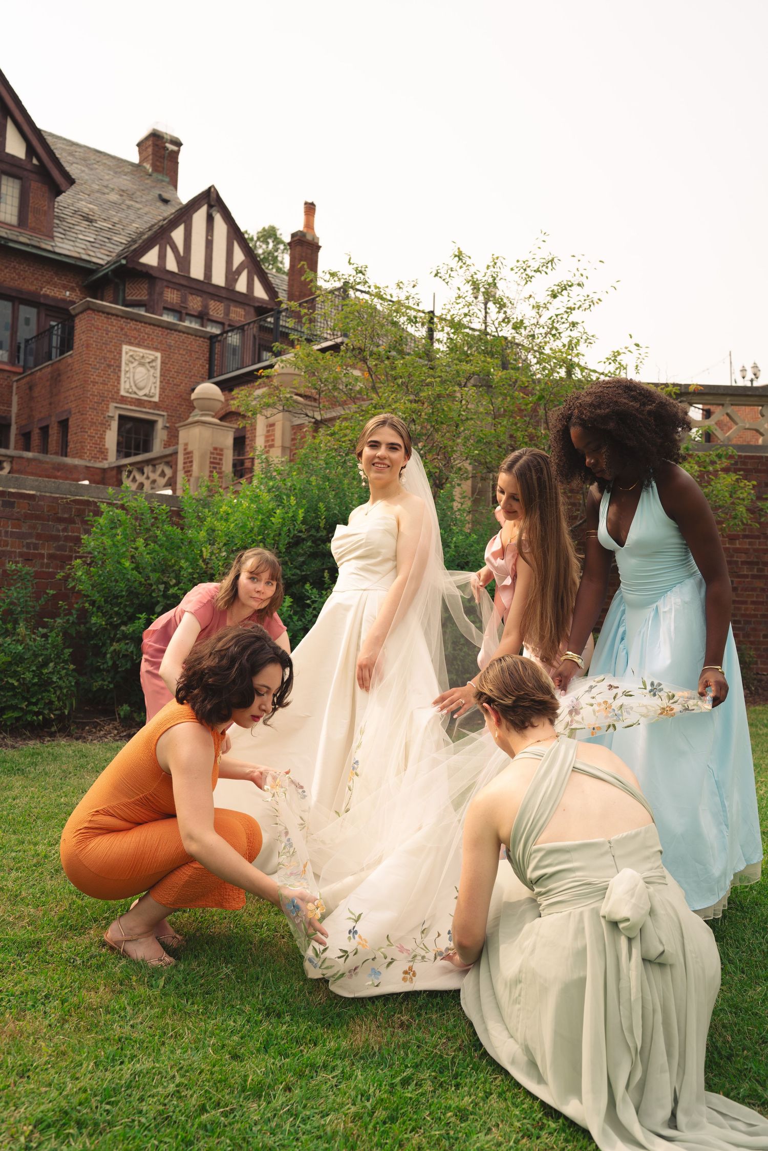Wedding party members playfully lift their dresses while posing in front of historic building.