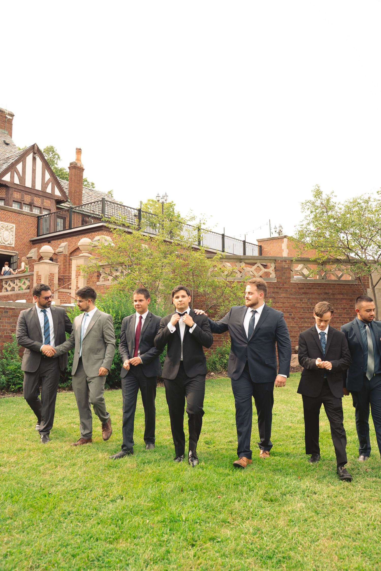 Groomsmen in suits pose playfully on grass during outdoor wedding photo session.