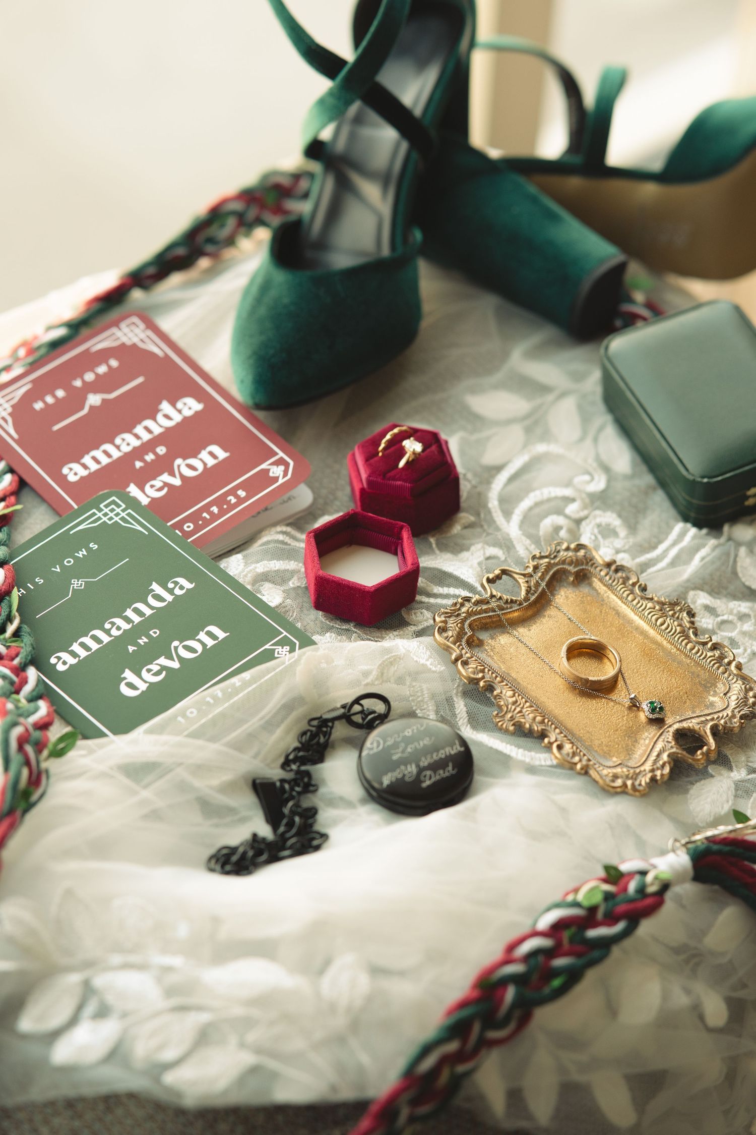 Wedding accessories including green and red details with jewelry boxes on lace fabric.