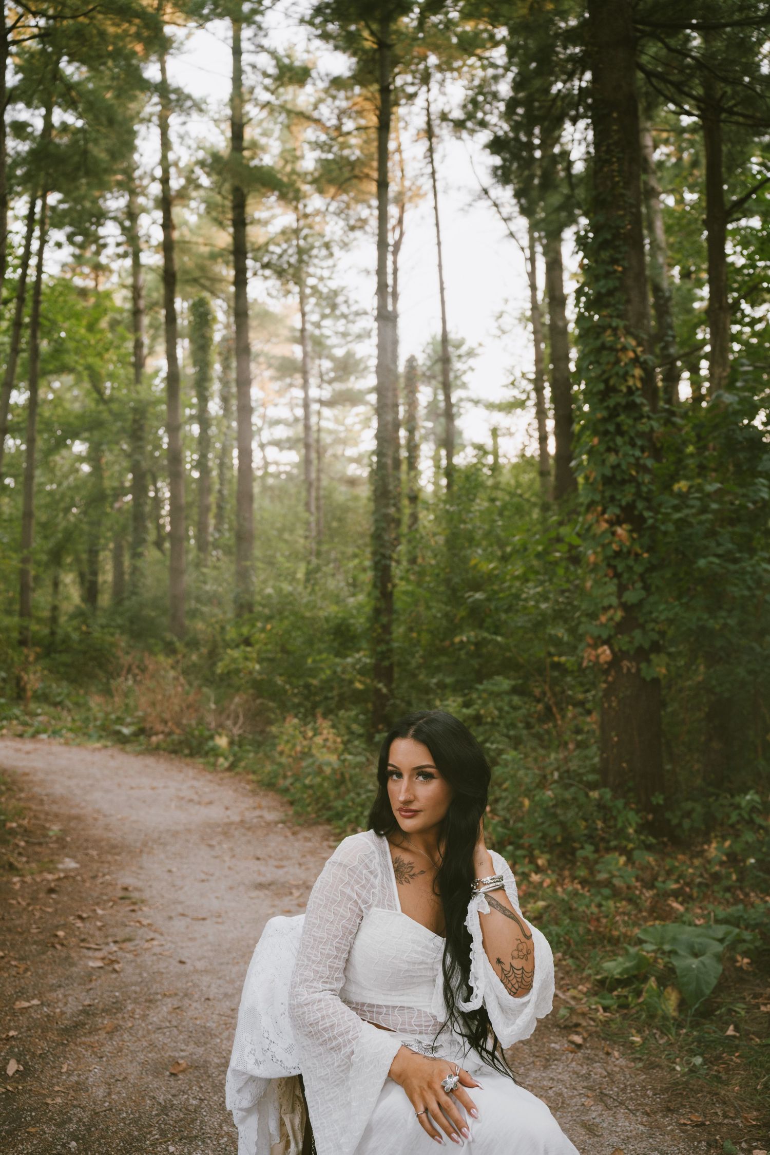 Woman in white dress poses gracefully on a forest path during autumn.