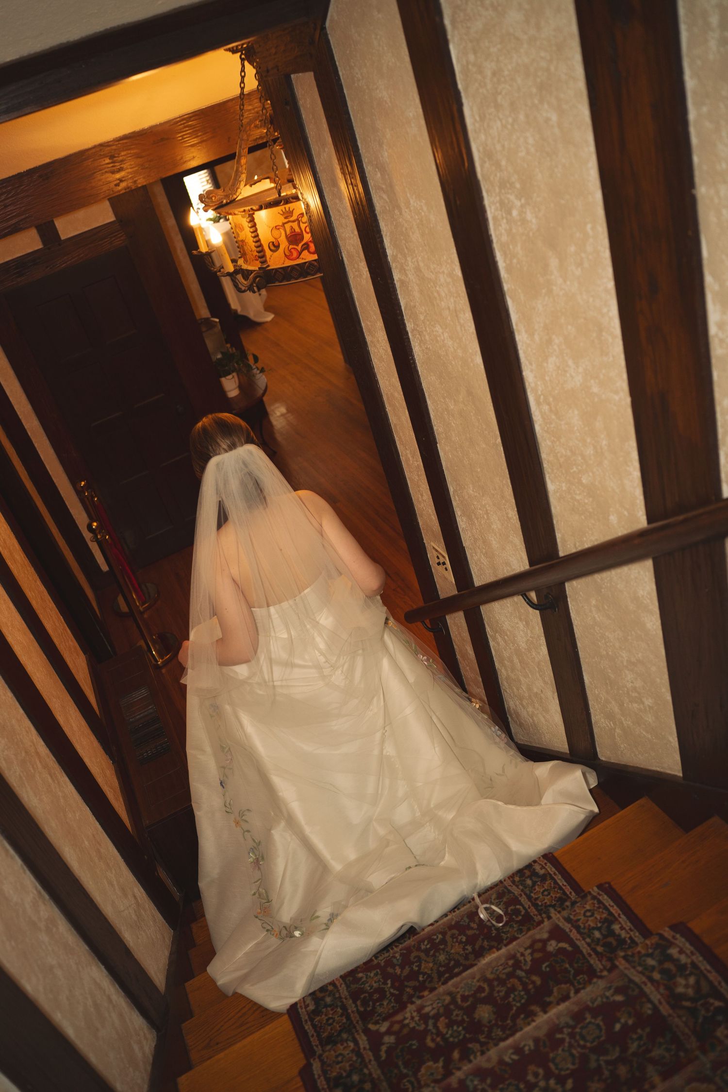 Bridal gown with flowing train photographed in warm-lit historic interior with wooden beams.