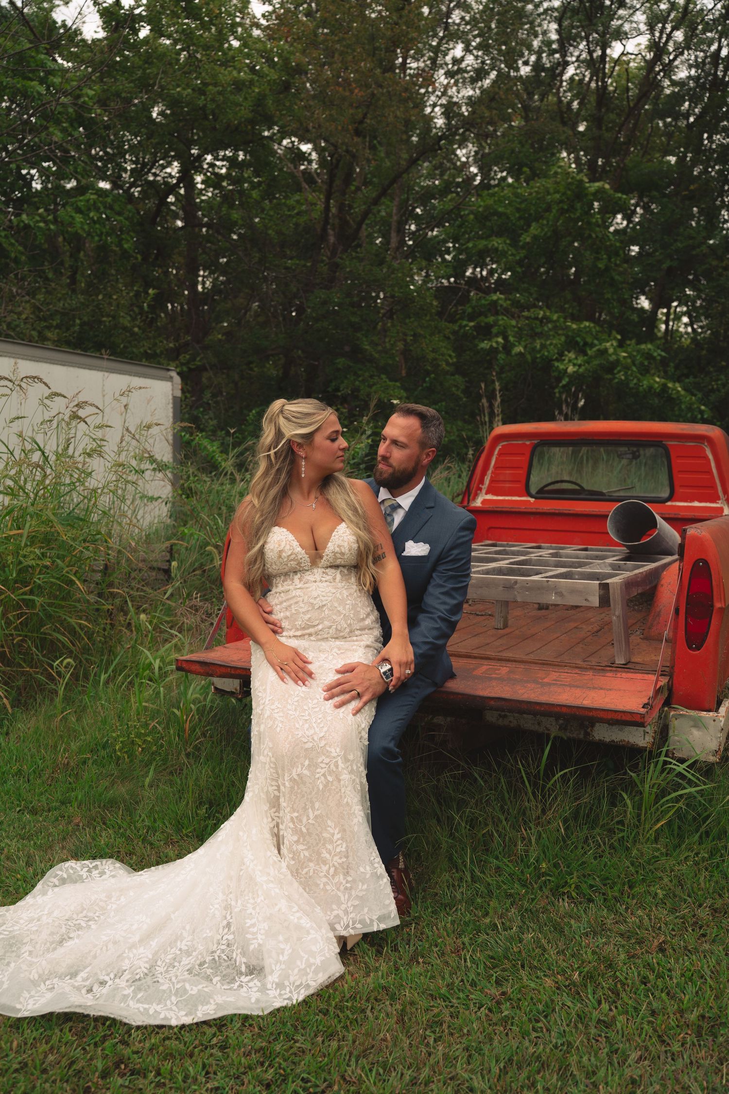 Newlyweds sharing candid moments near rustic red truck in outdoor setting.
