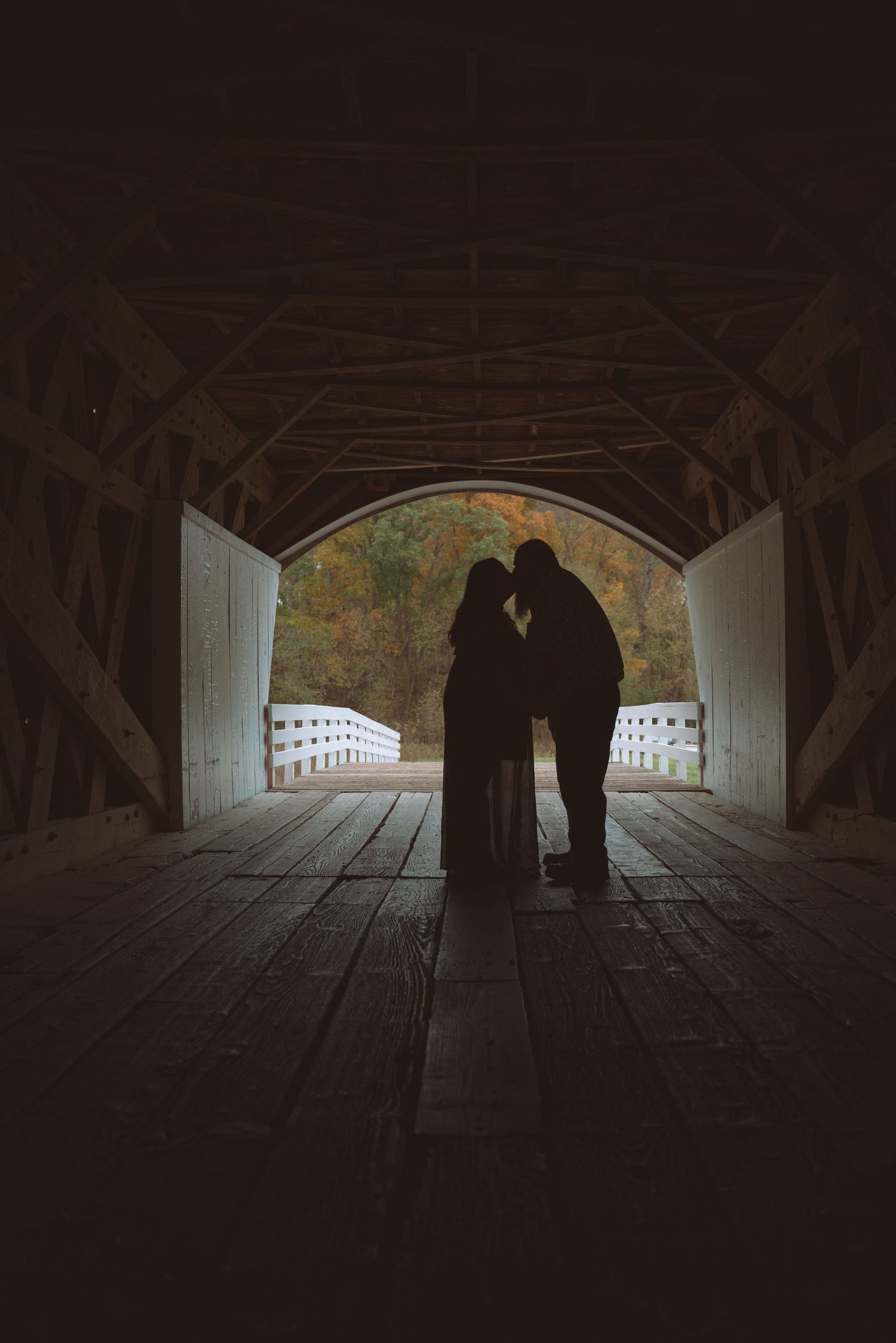 Silhouettes of figures walking through a dark covered bridge with light visible at both ends.