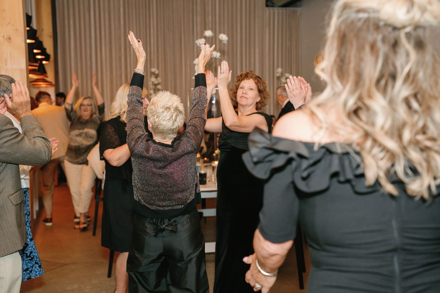 Guests dancing with arms raised at an elegant indoor wedding reception celebration.