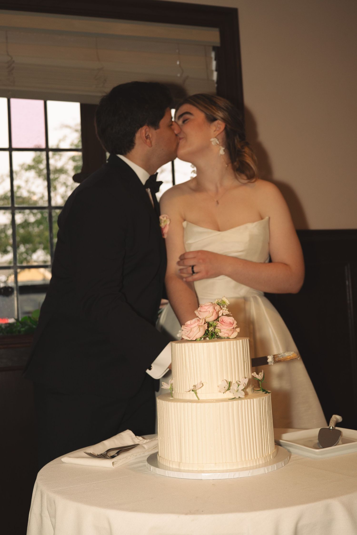Traditional cake cutting moment at wedding reception with white tiered cake.