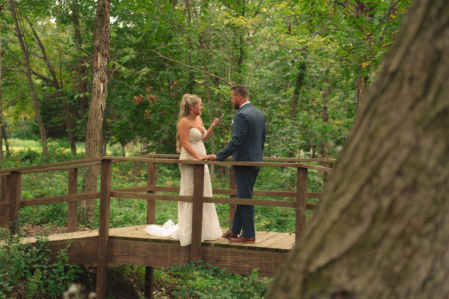 Wedding couple embracing on a rustic wooden walkway surrounded by lush greenery.