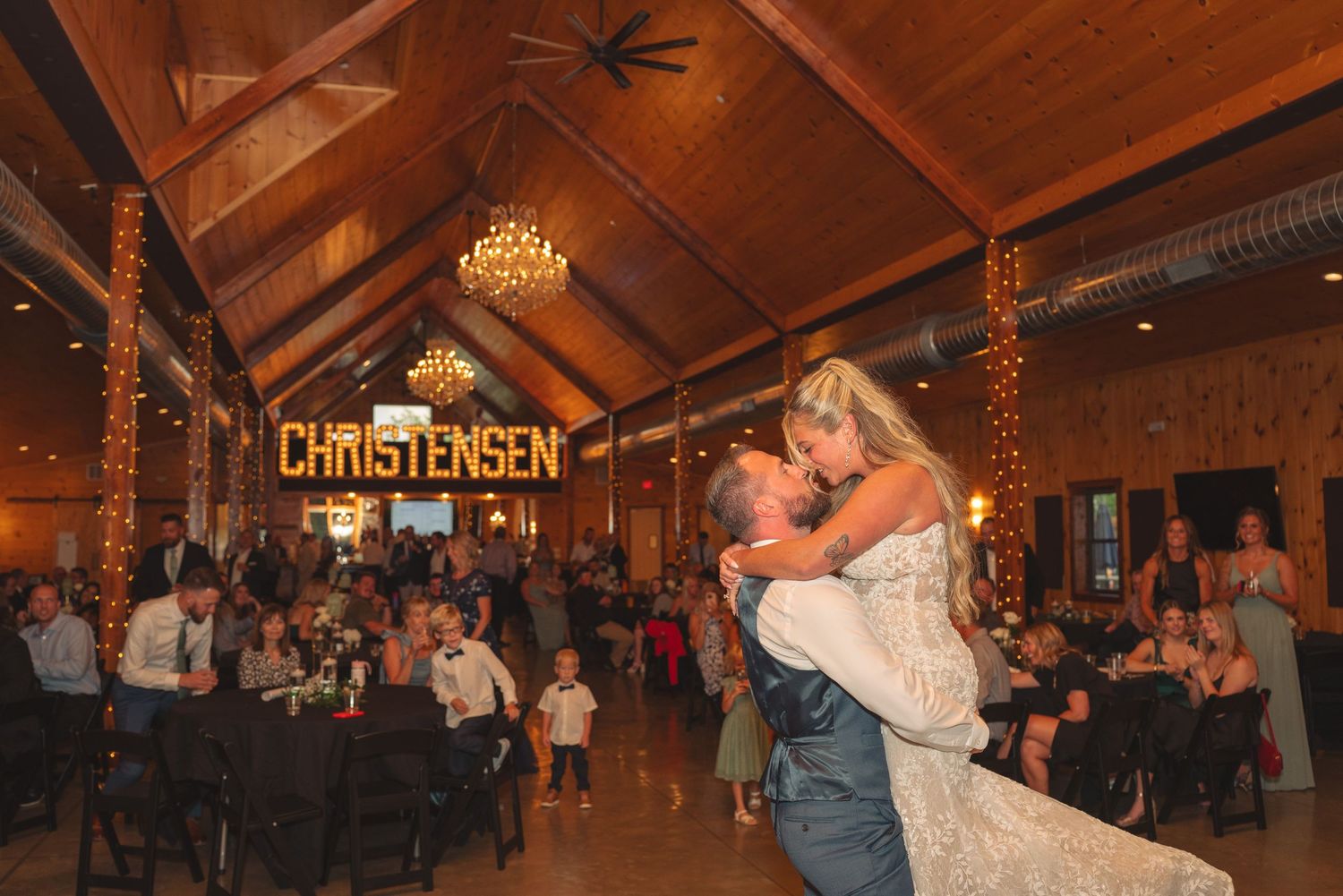 Wedding reception in rustic wooden venue with exposed beams and chandeliers.