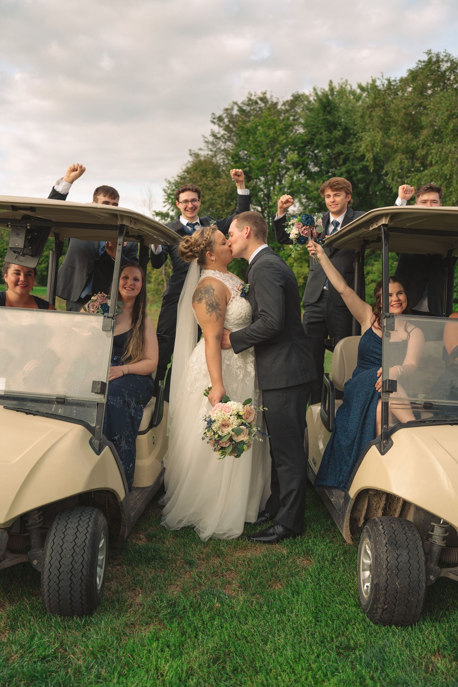 Wedding party posing playfully next to golf carts on grassy field.