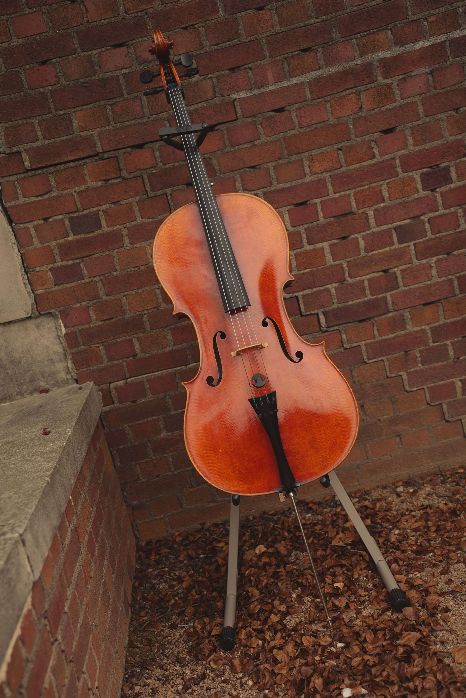 A wooden cello rests against red brick wall during an outdoor event.