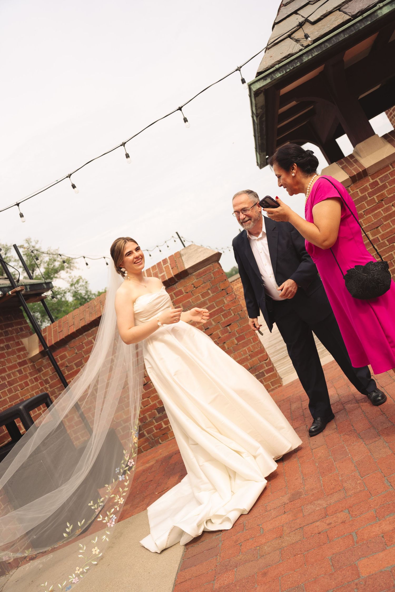 Wedding party celebrates on brick patio with string lights overhead.