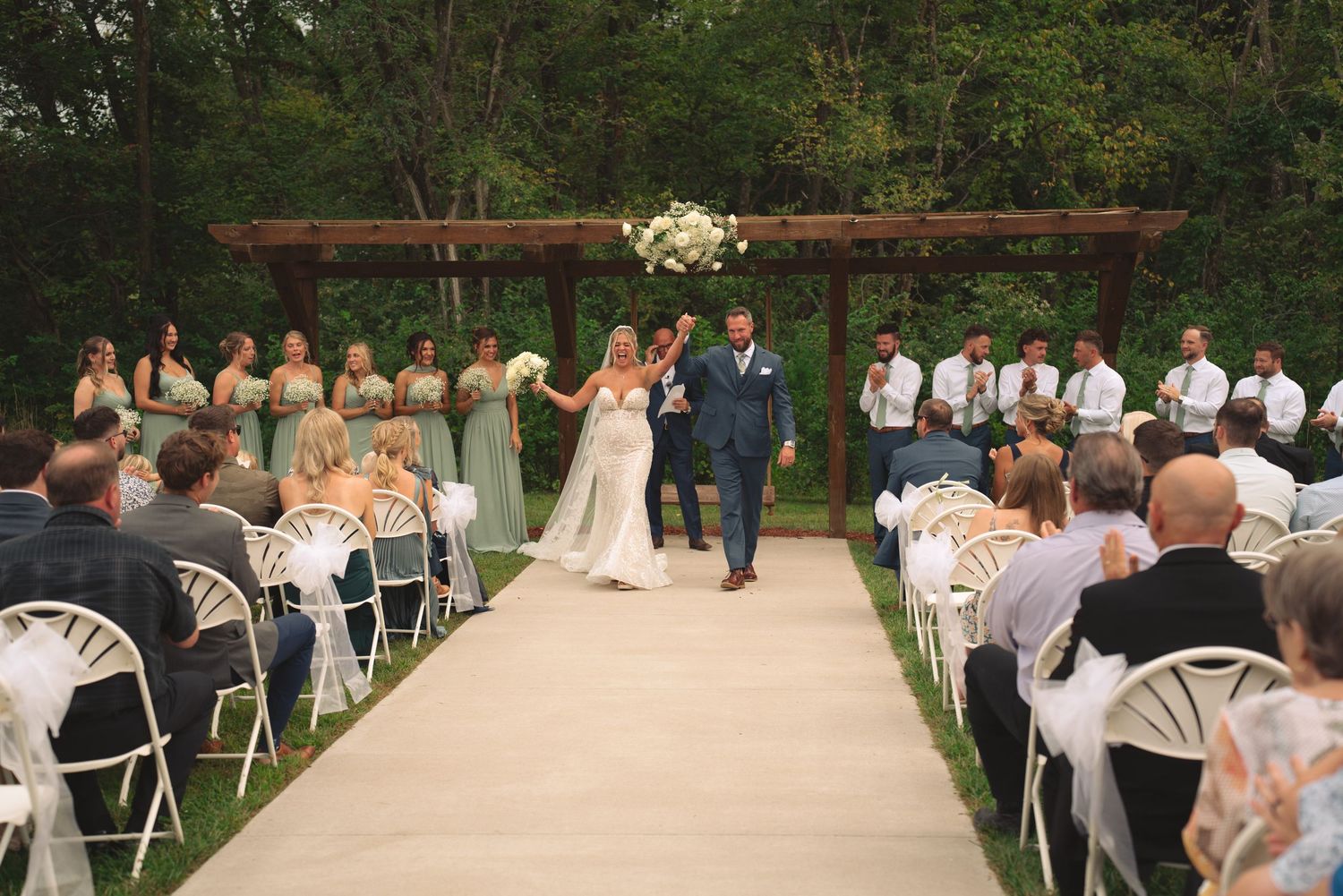 Wedding guests seated in white chairs during an outdoor garden ceremony.
