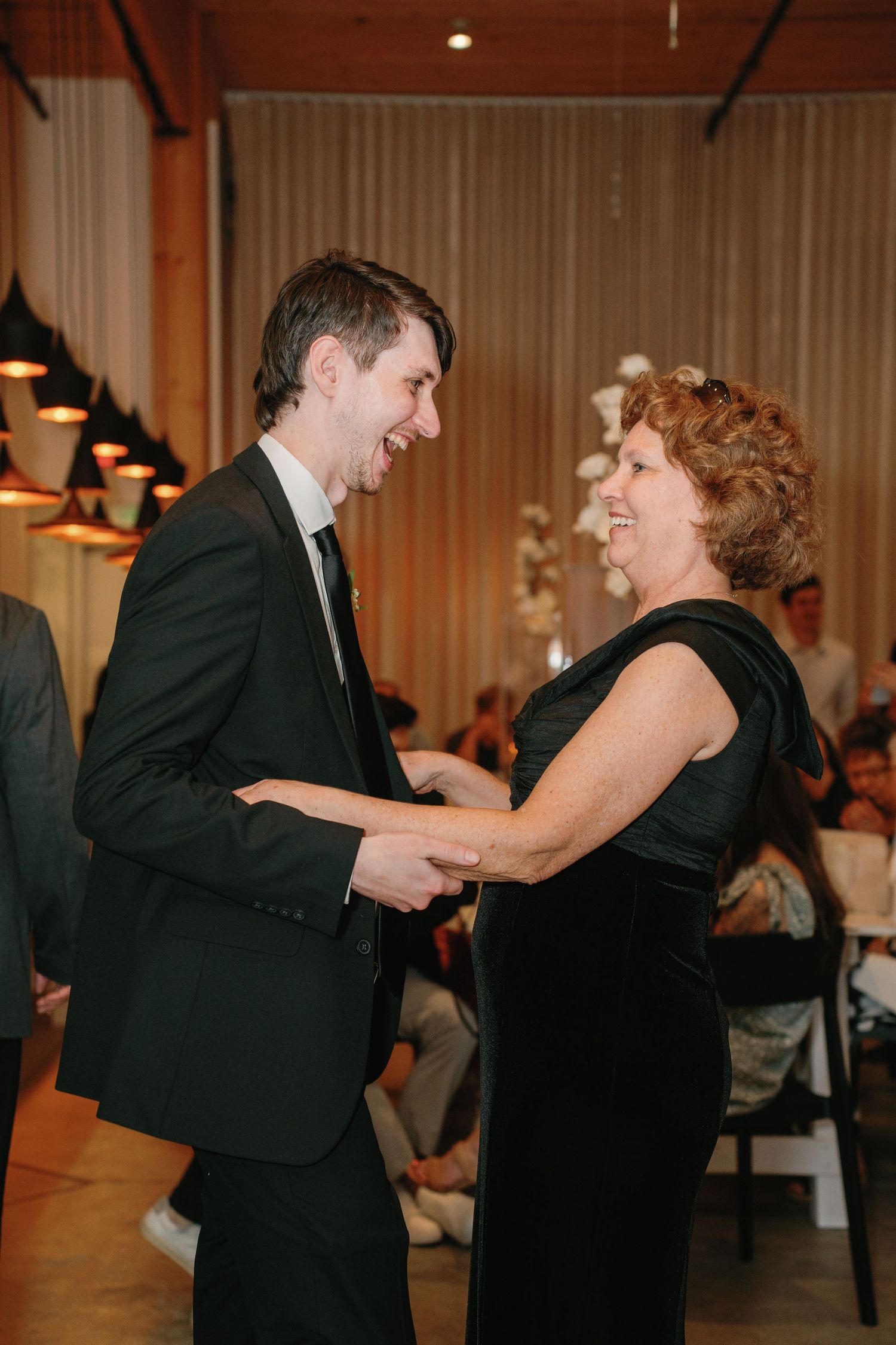 A man in a black suit and woman in black dress share a joyful dance together at an elegant wedding reception.