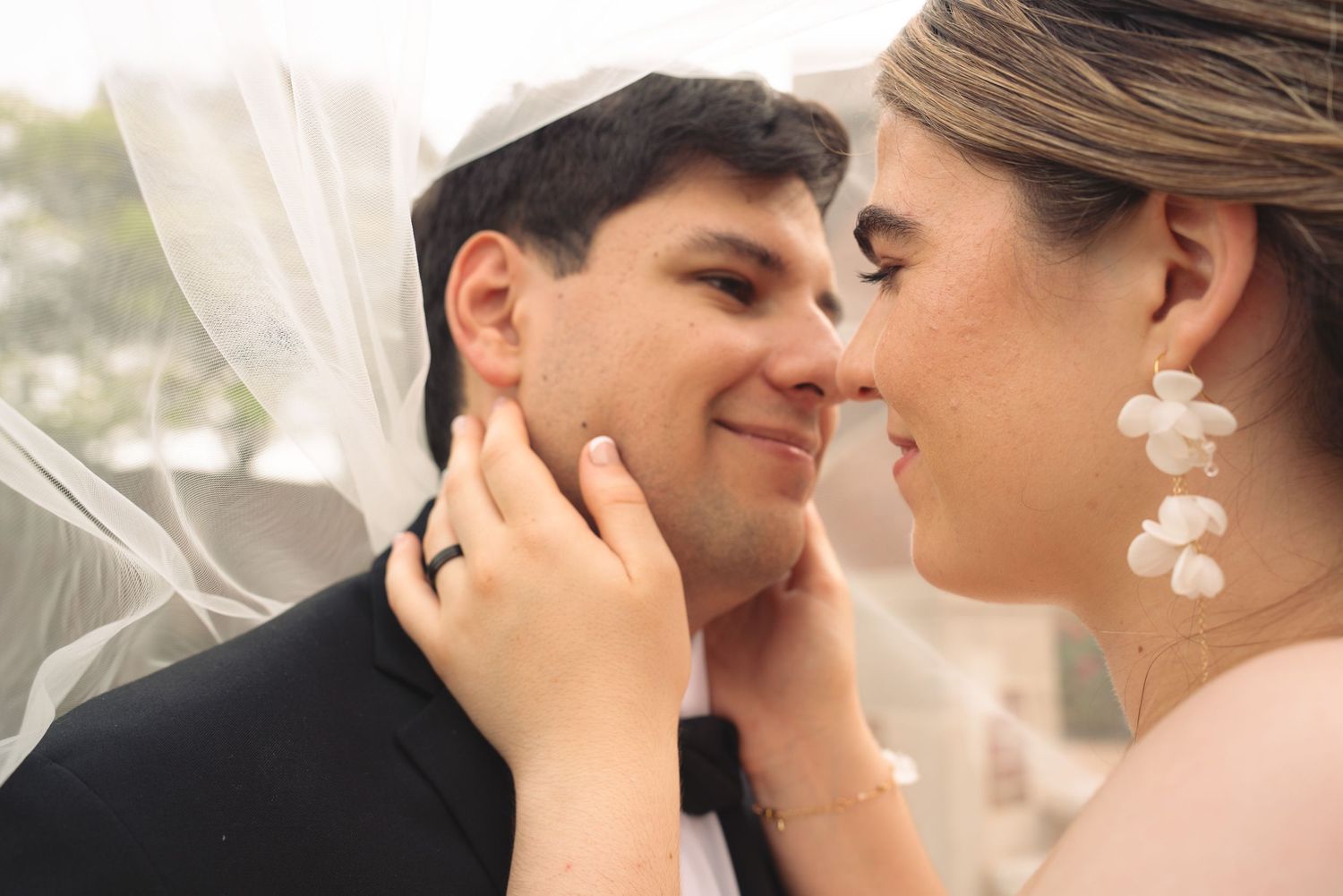 Intimate close-up of newlyweds sharing a tender moment with the bride wearing floral earrings.