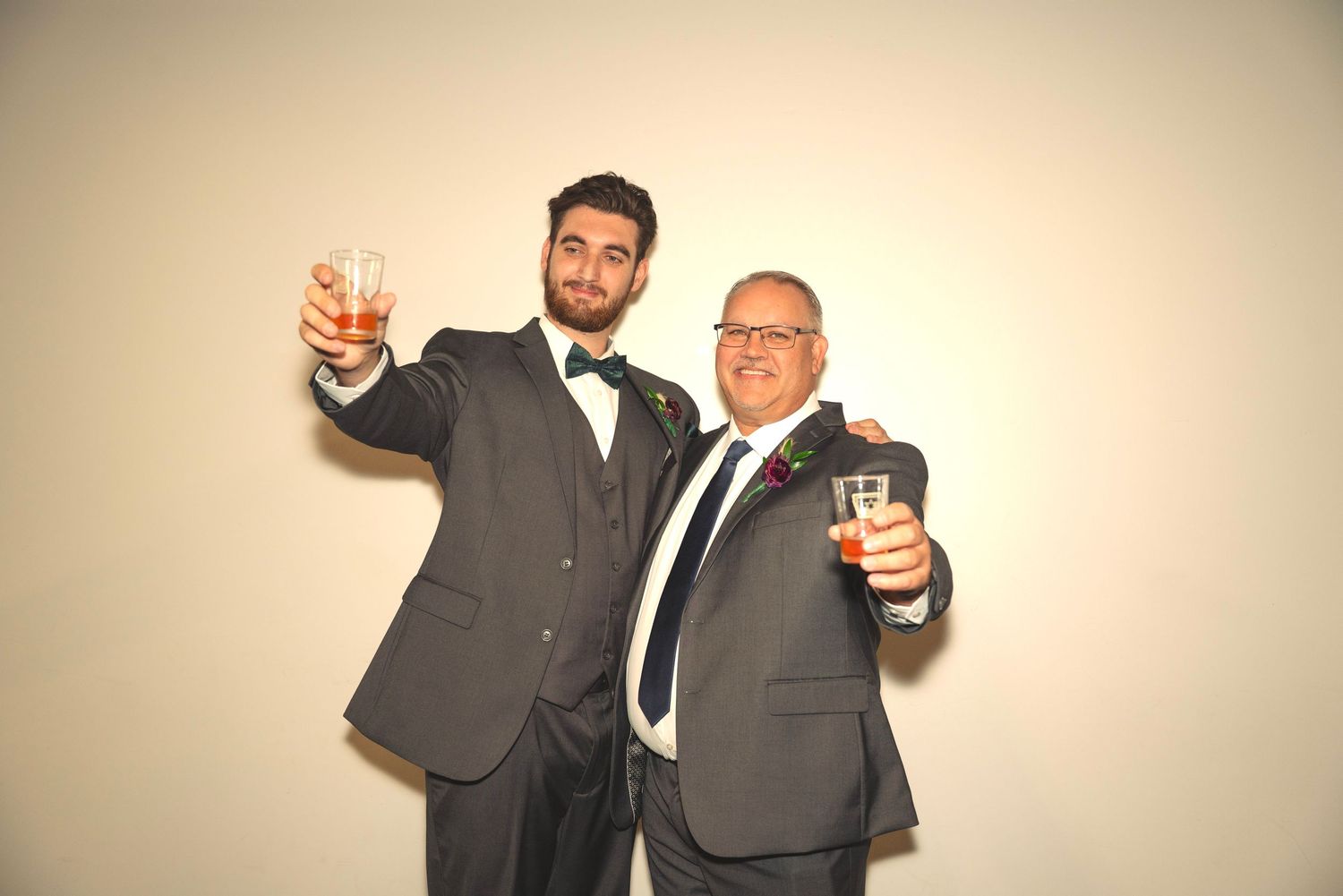 Groomsmen in dark suits posing against light background at wedding celebration.