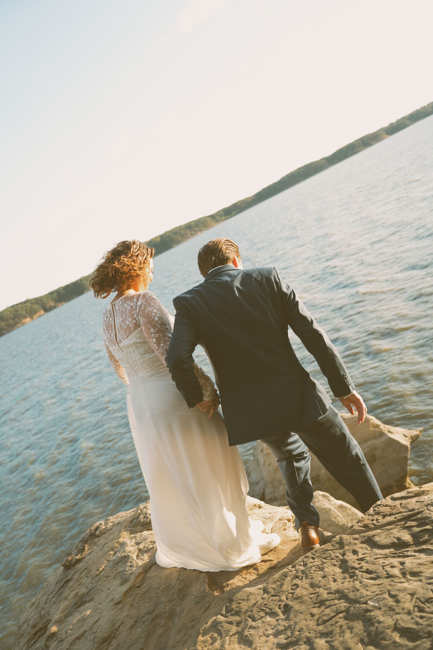 Couple sits together watching sunset on rocky beach shore.