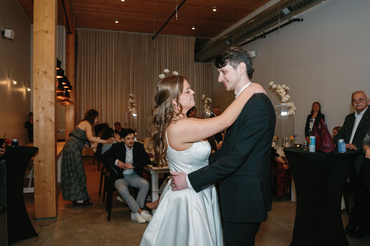 Bride and groom share their first dance at a modern wedding reception venue with guests seated in background.