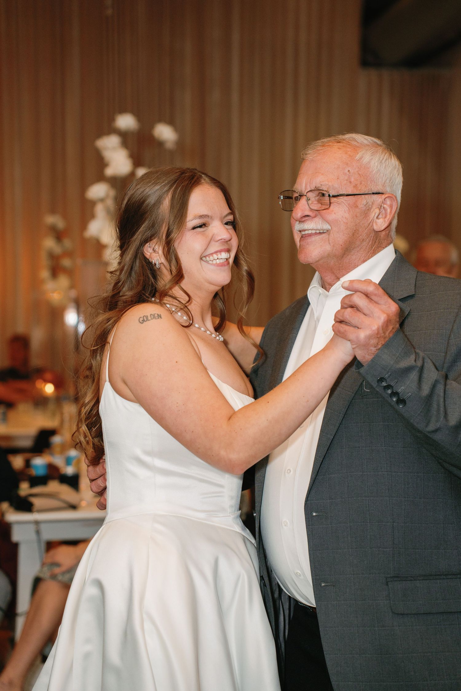 Bride in white gown sharing a joyful father-daughter dance at wedding reception.