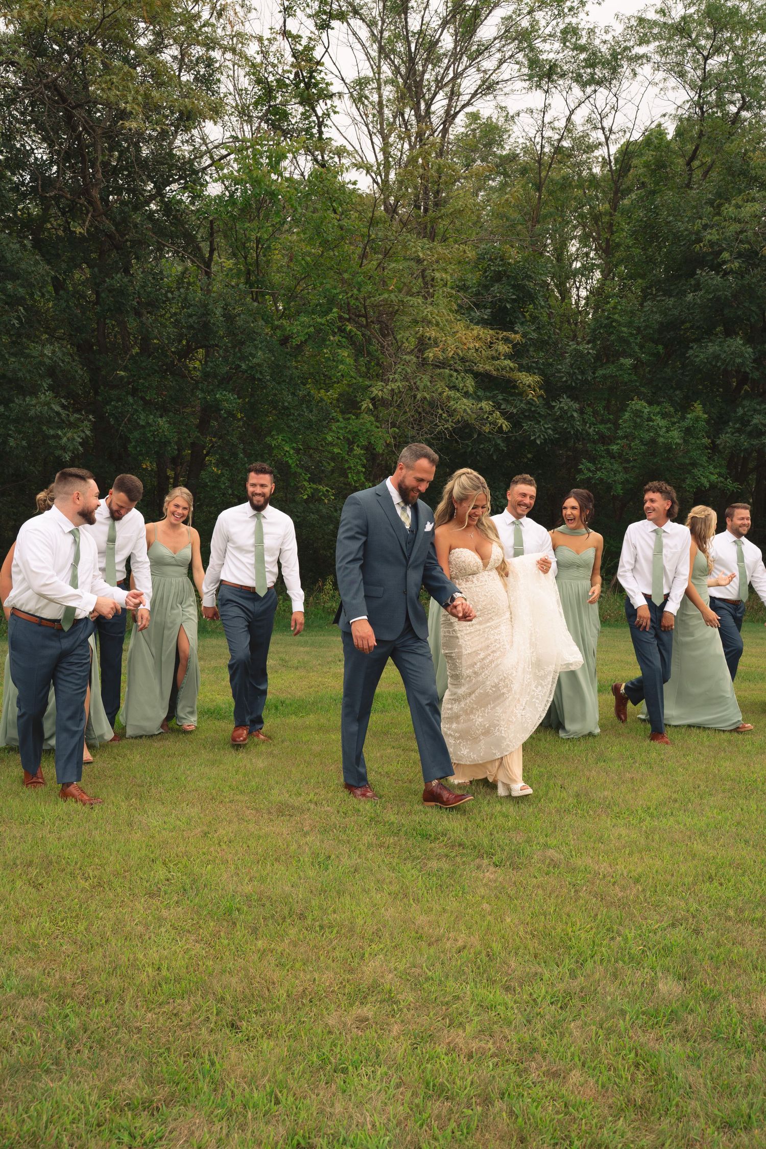 Wedding party creates playful domino effect pose in a grassy outdoor setting.