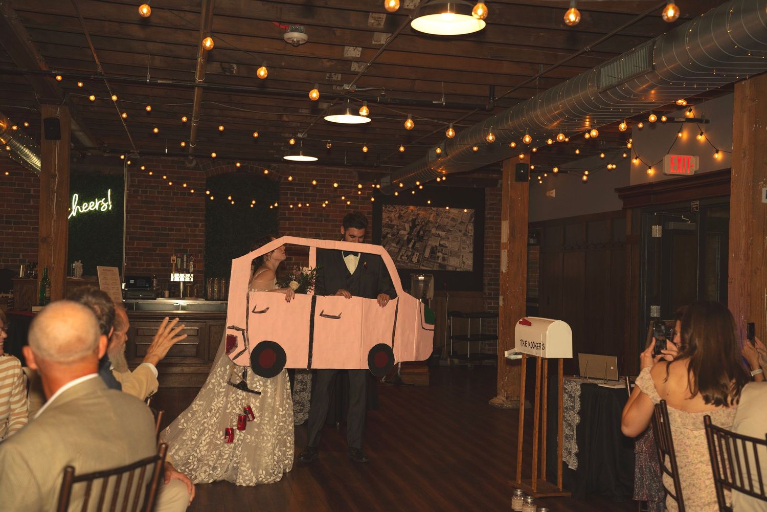 Wedding reception venue with string lights and exposed brick walls filled with guests.