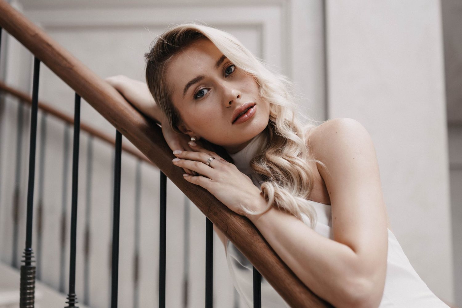 Elegant figure poses gracefully on a staircase railing in a soft, romantic indoor setting.