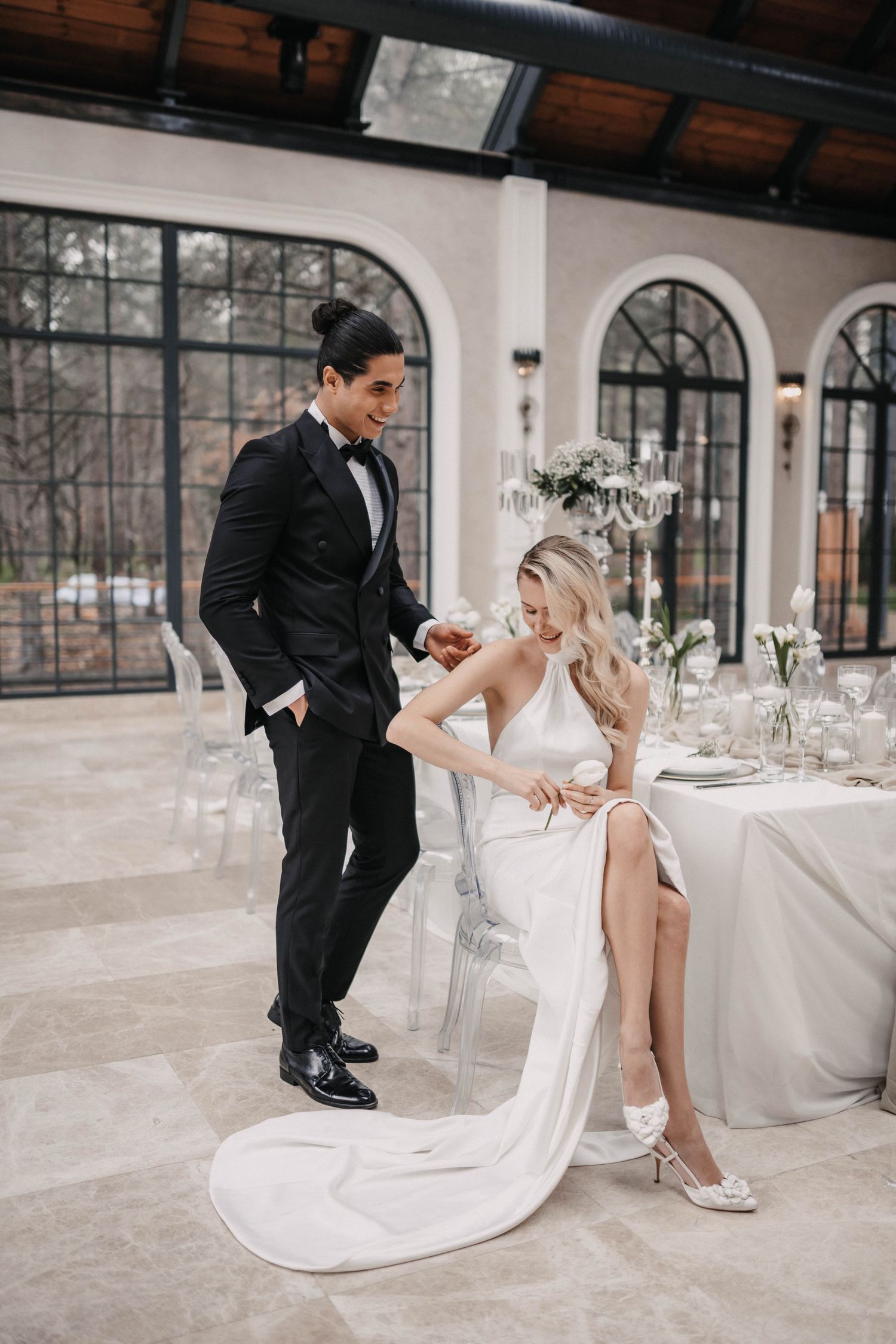 Elegant wedding couple sharing a moment in venue with arched windows and white table settings.