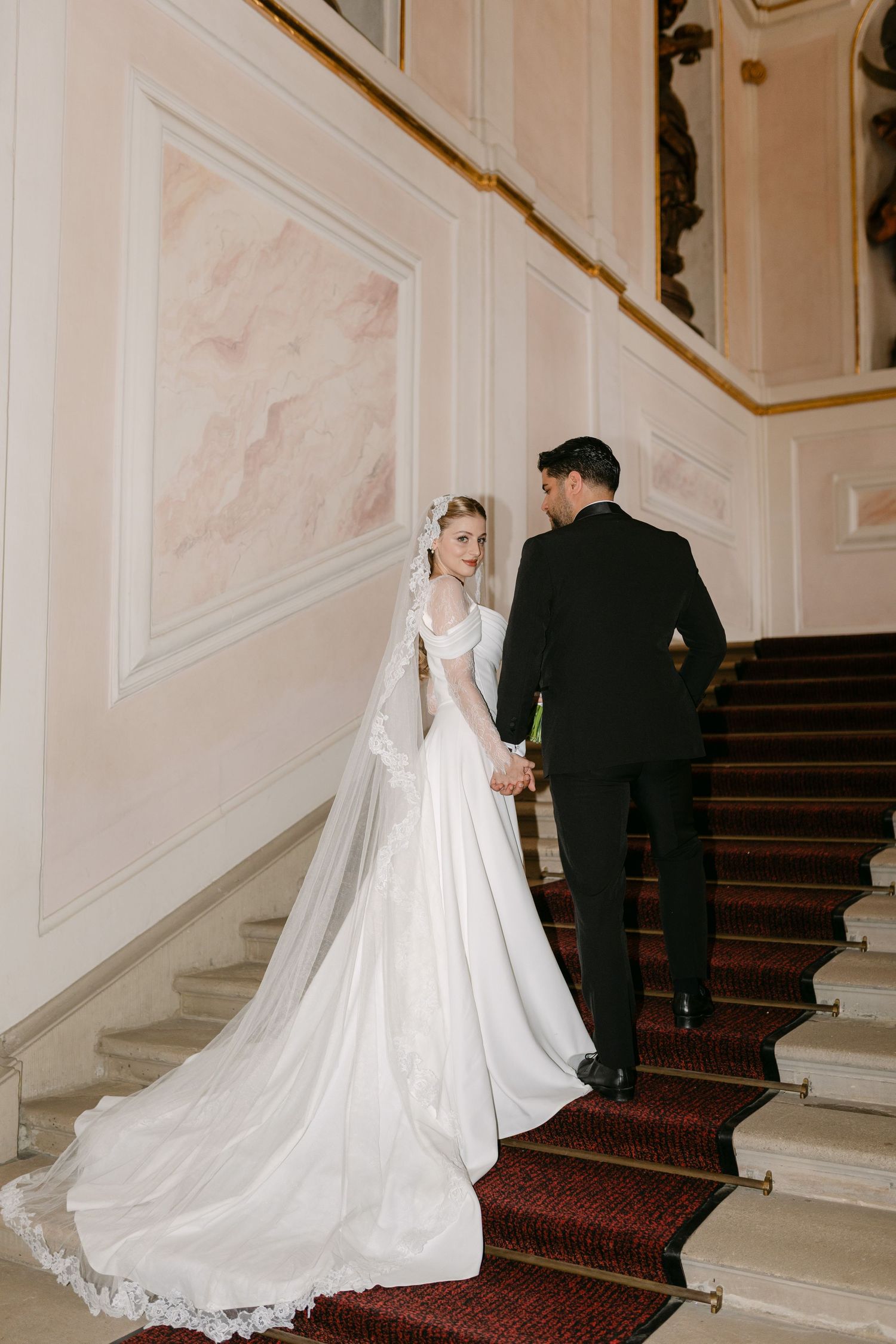 Wedding couple ascending grand staircase with flowing white dress train.