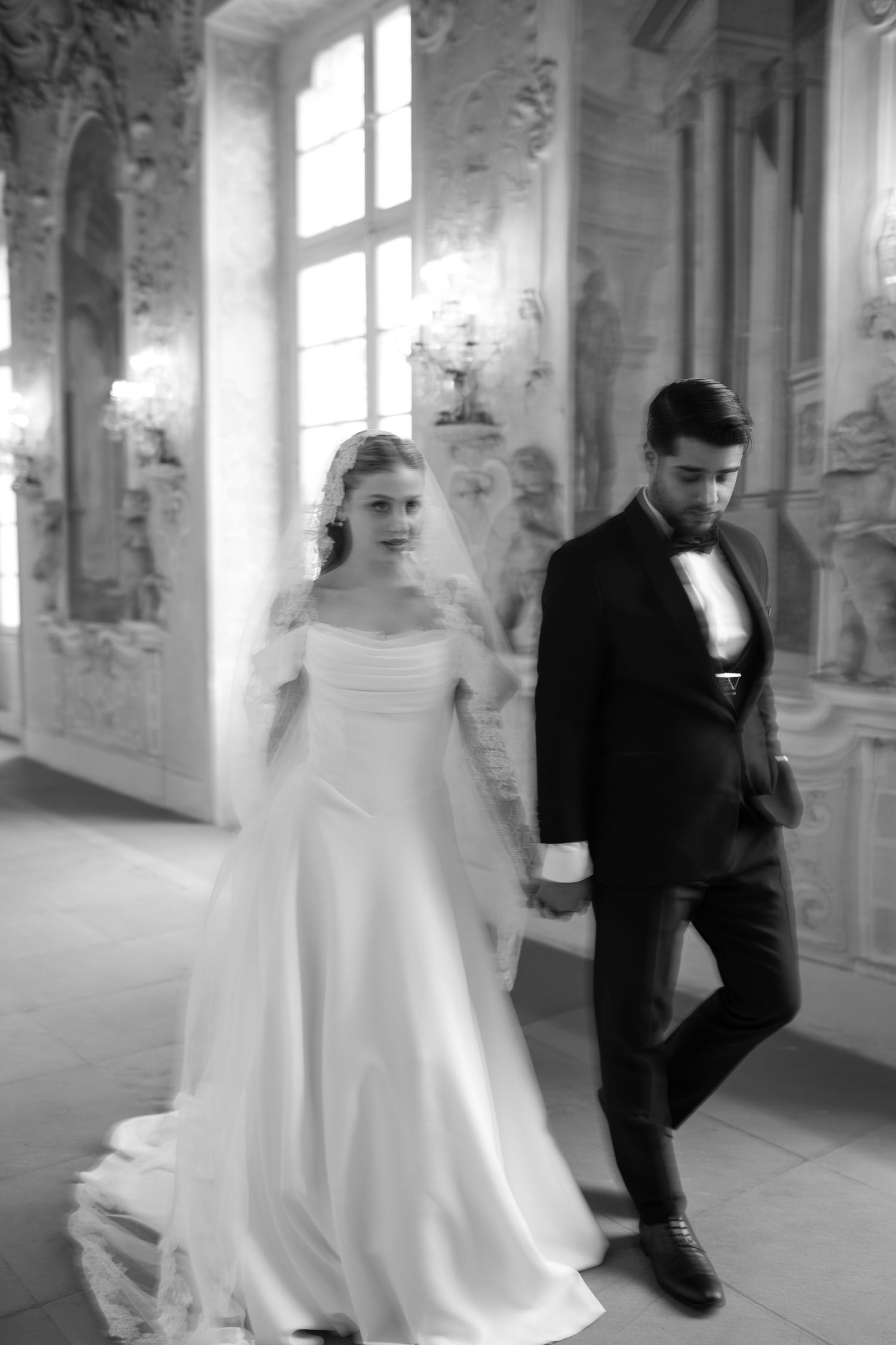 Wedding couple walking through ornate hallway with classical architecture and windows.