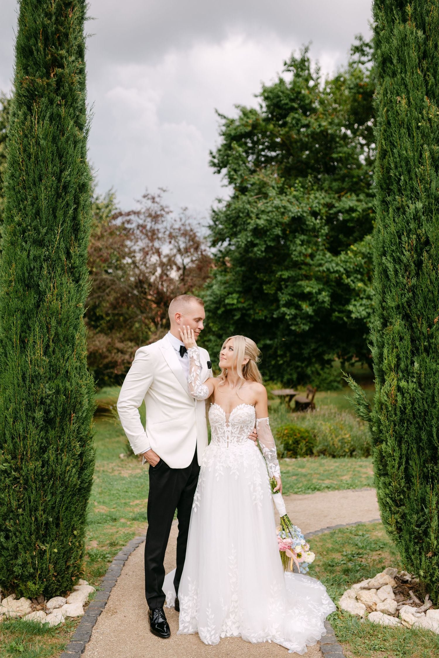 Newlyweds share a romantic moment on a stone-lined pathway surrounded by greenery.