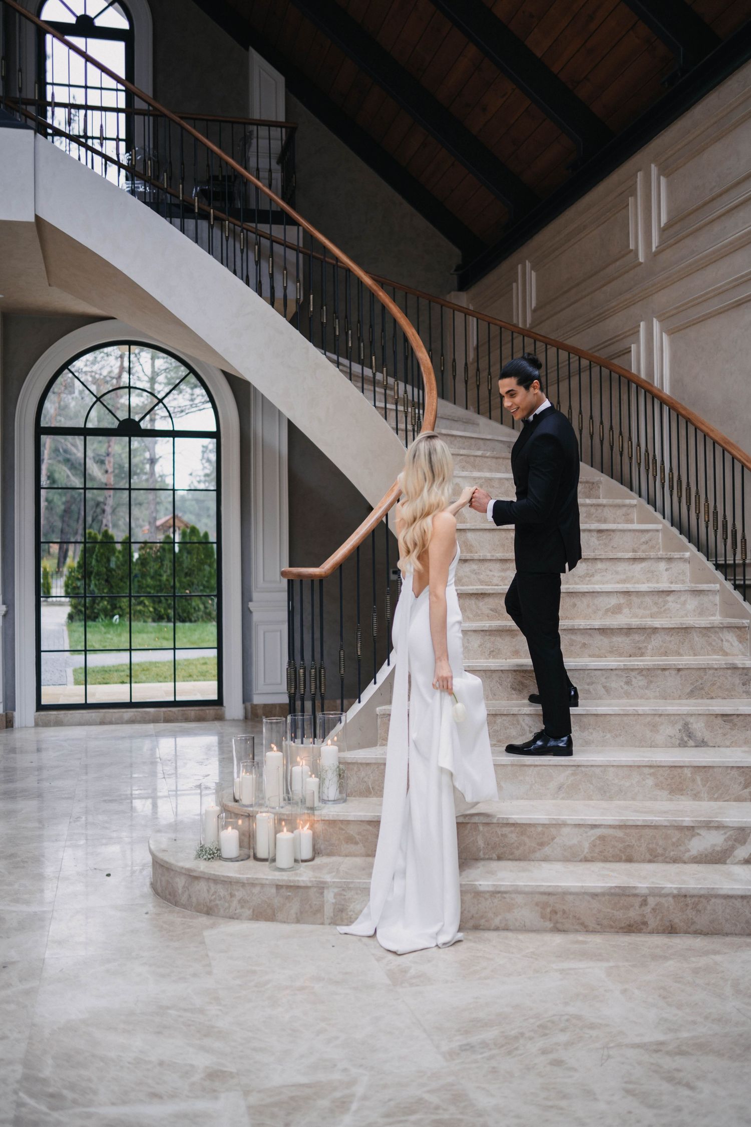 Couple in formal attire pose dramatically on grand marble staircase with candles.