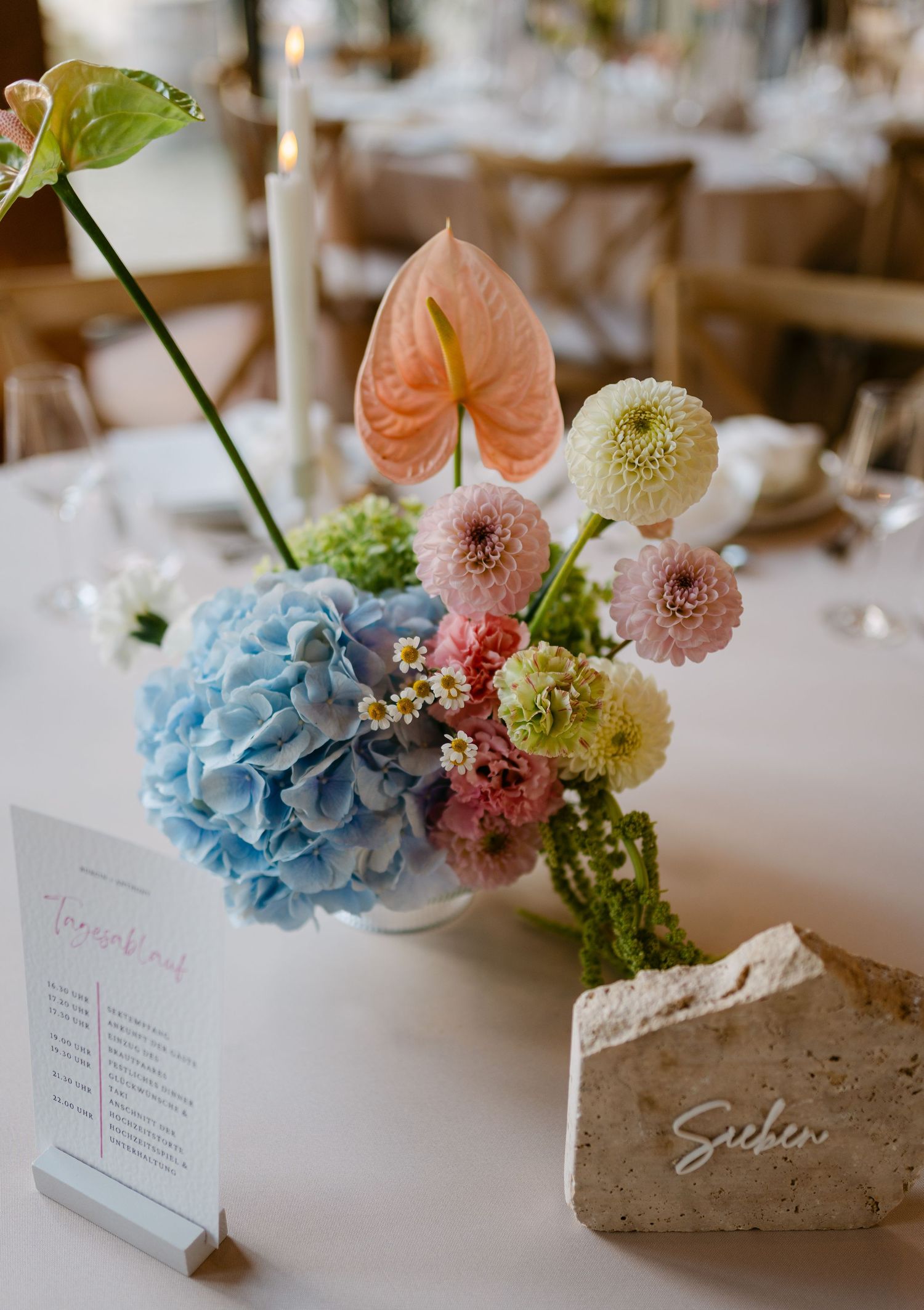Elegant wedding centerpiece featuring blue hydrangeas and pink flowers in a stone vase with place cards.