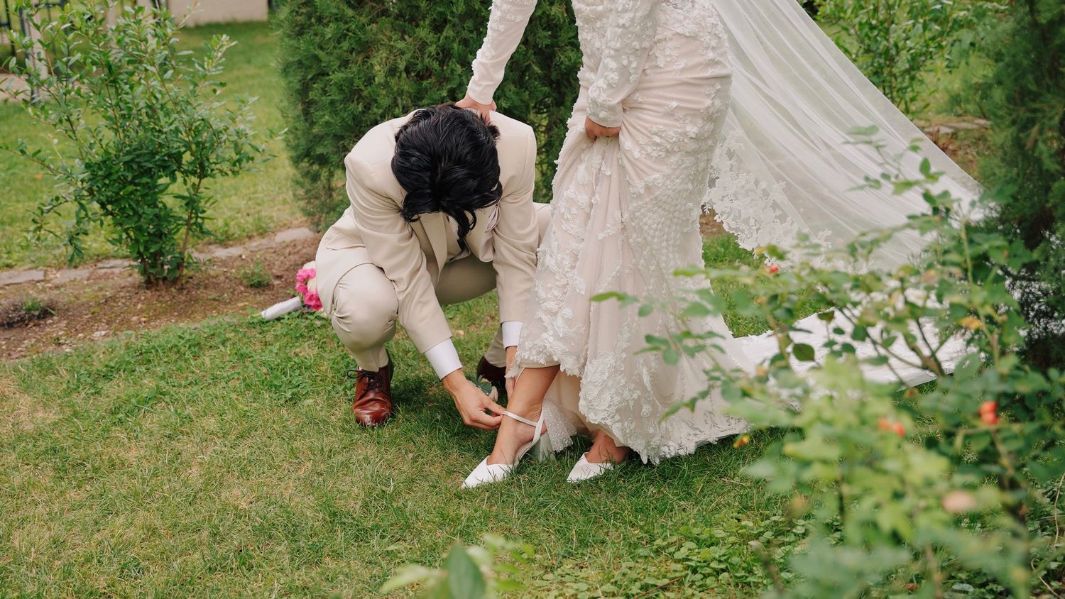 Wedding couple walking through a lush garden pathway with greenery.