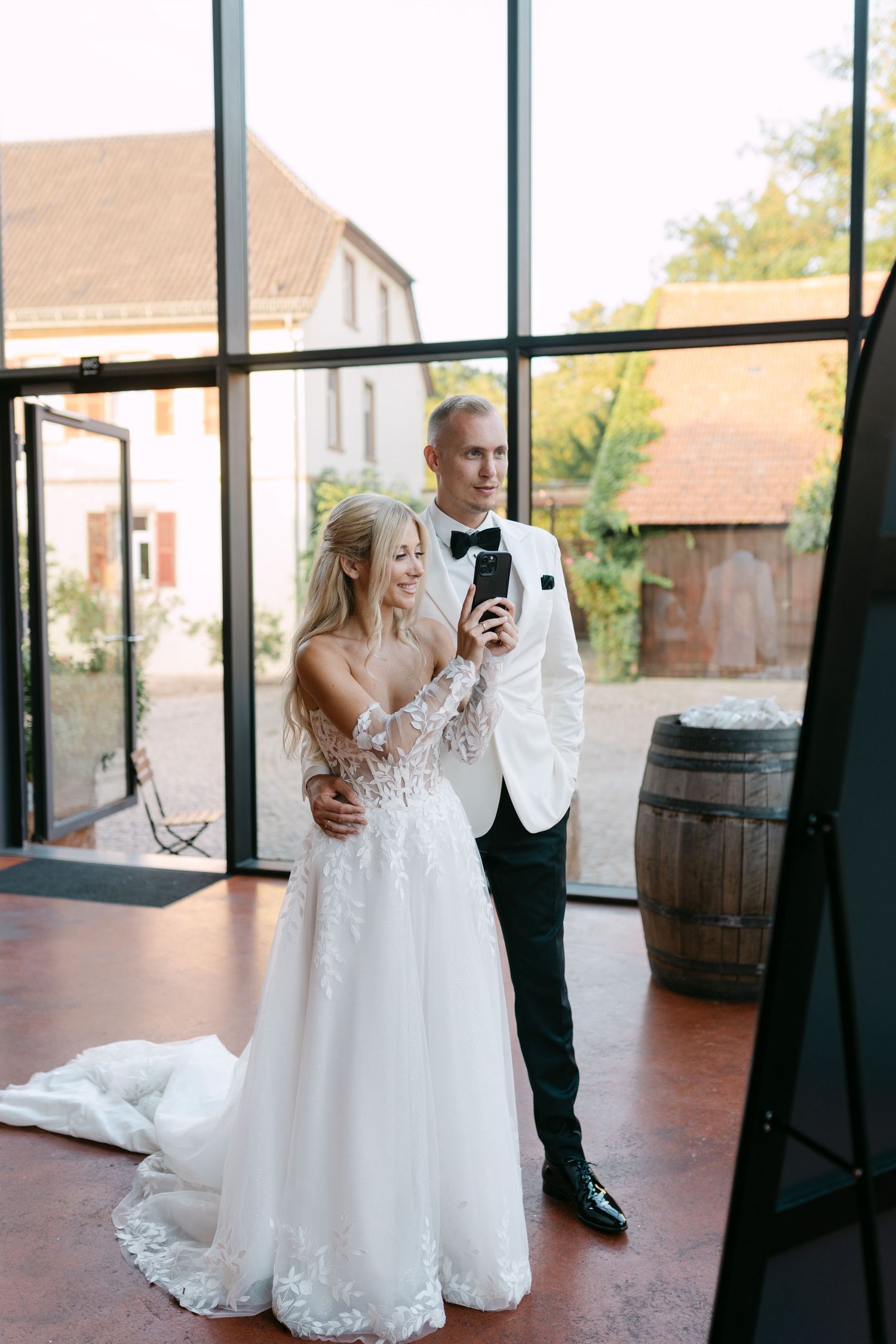 Couple checking their phones in a modern venue with large windows and wooden barrels.