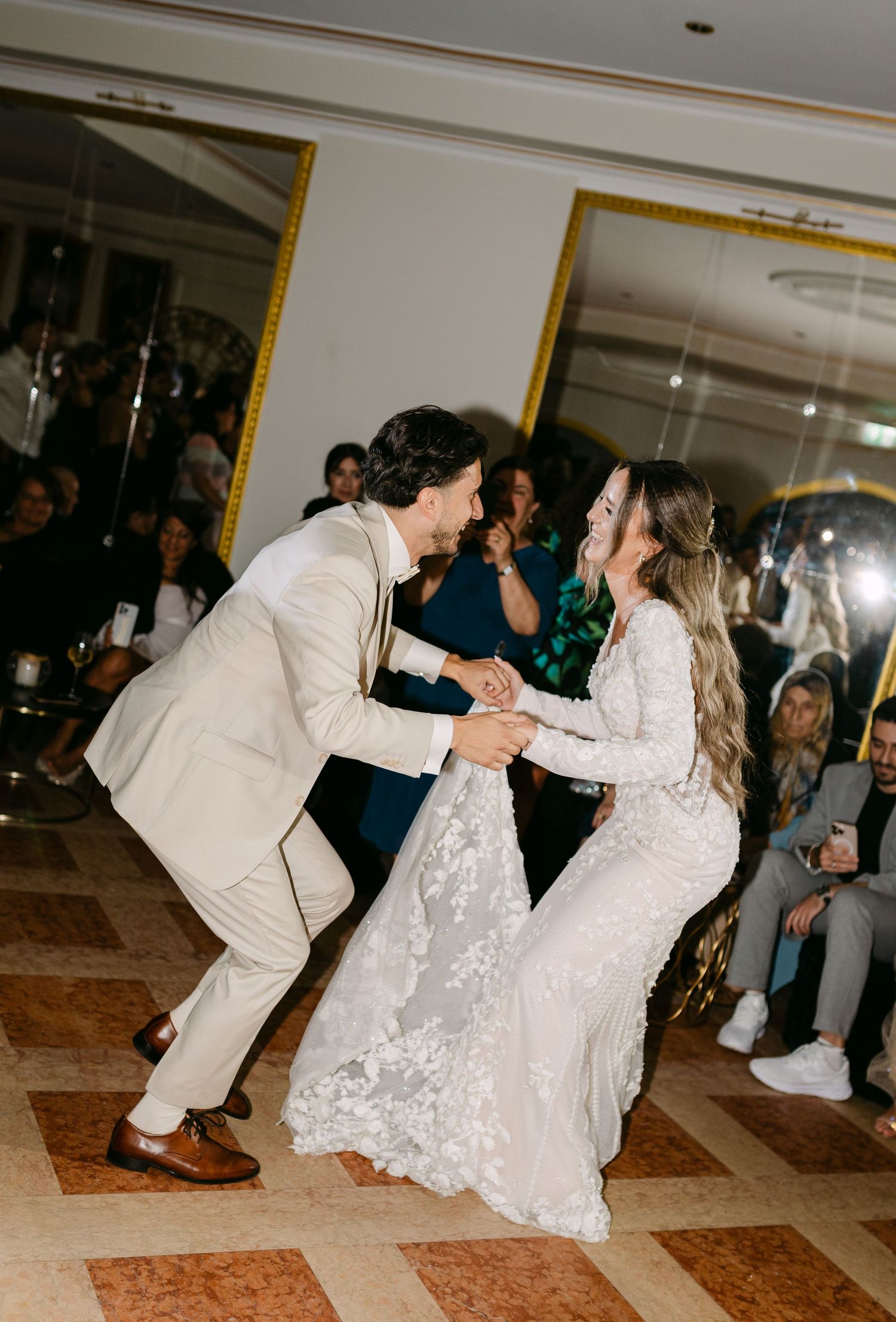 Wedding couple performing energetic dance moves on marble floor at reception.