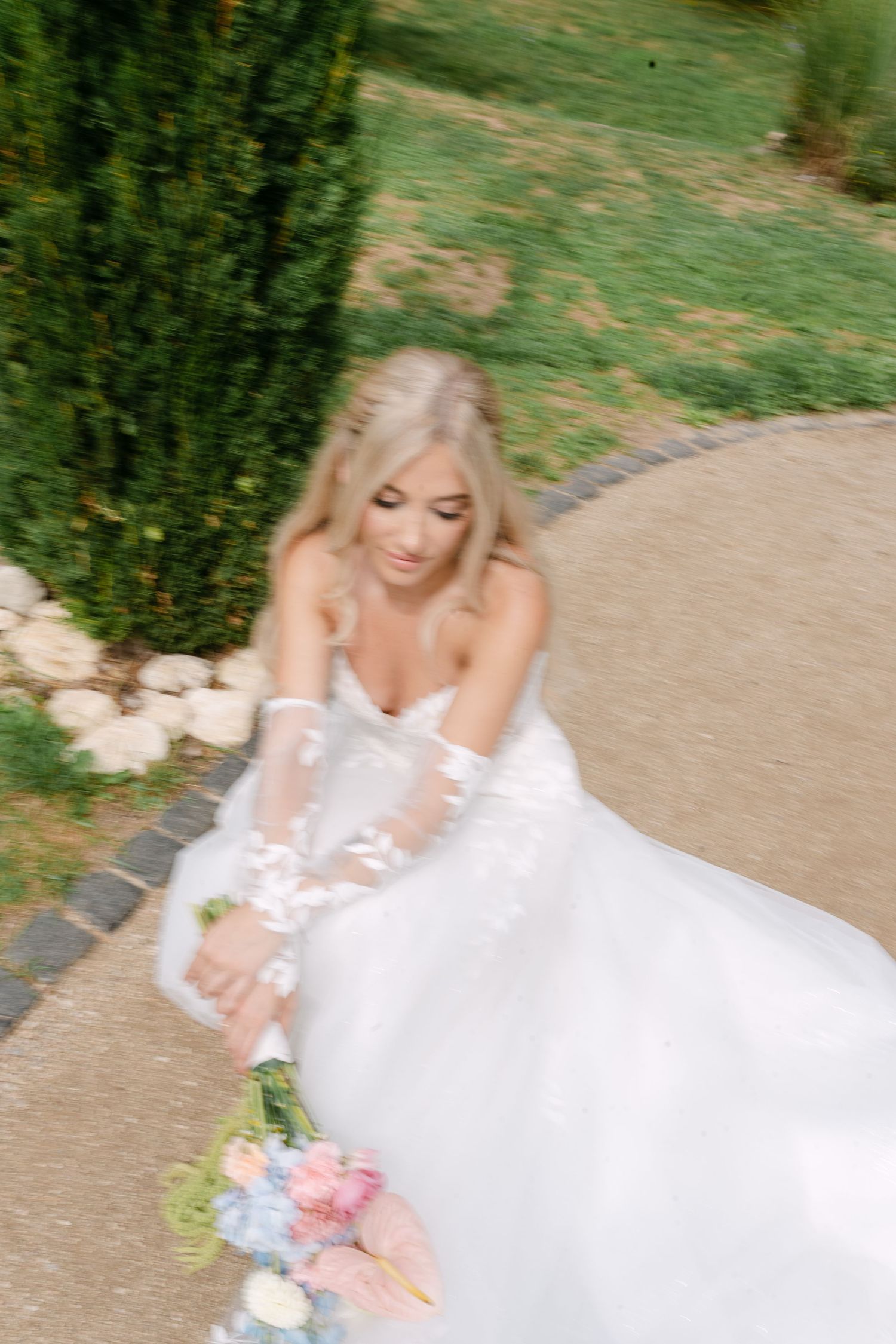 Bride in flowing white dress sitting gracefully in an outdoor garden setting.