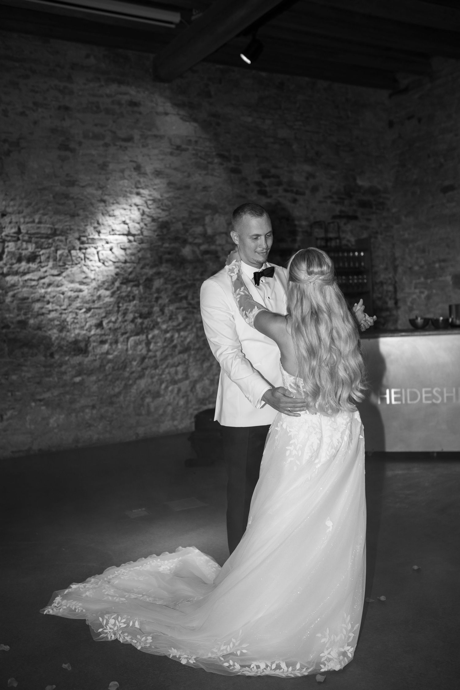 A couple dances together in a rustic brick-walled venue during their wedding reception.
