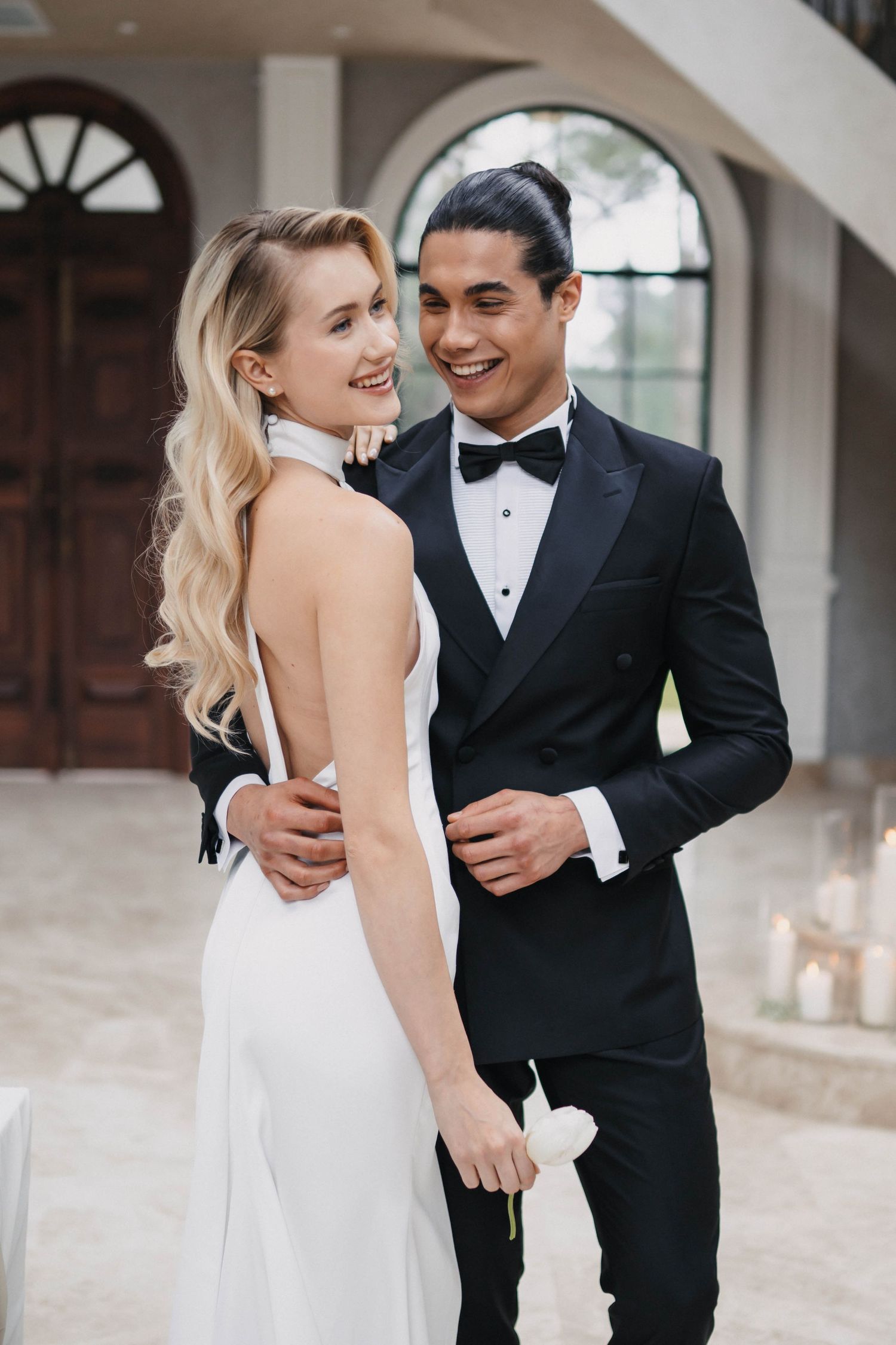 Elegant wedding couple sharing intimate moments in a bright hallway with arched windows.