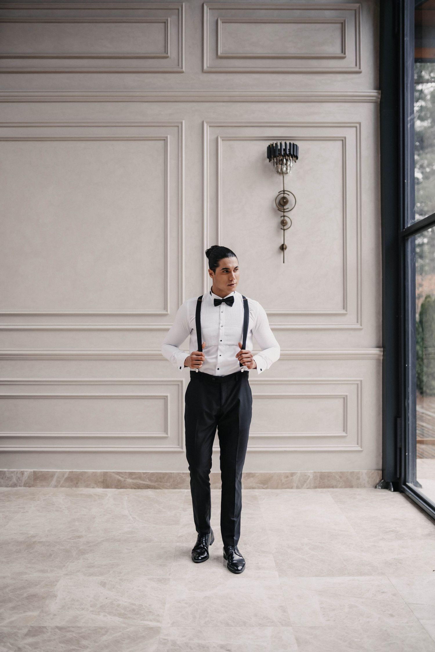 Classic formal attire with bow tie and suspenders against elegant white paneled wall.