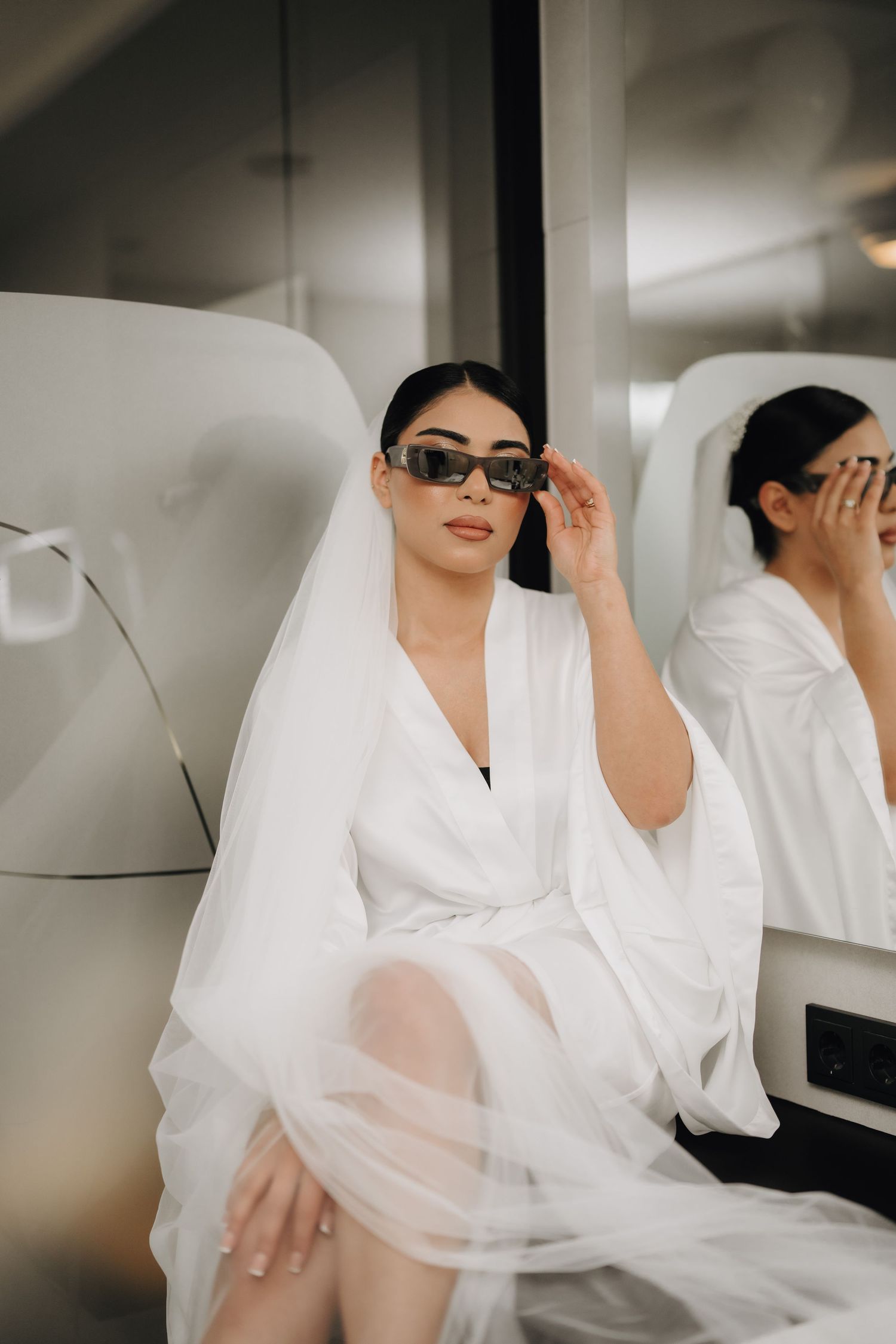Artistic black and white photo of wedding preparations with flowing white fabric and sunglasses.
