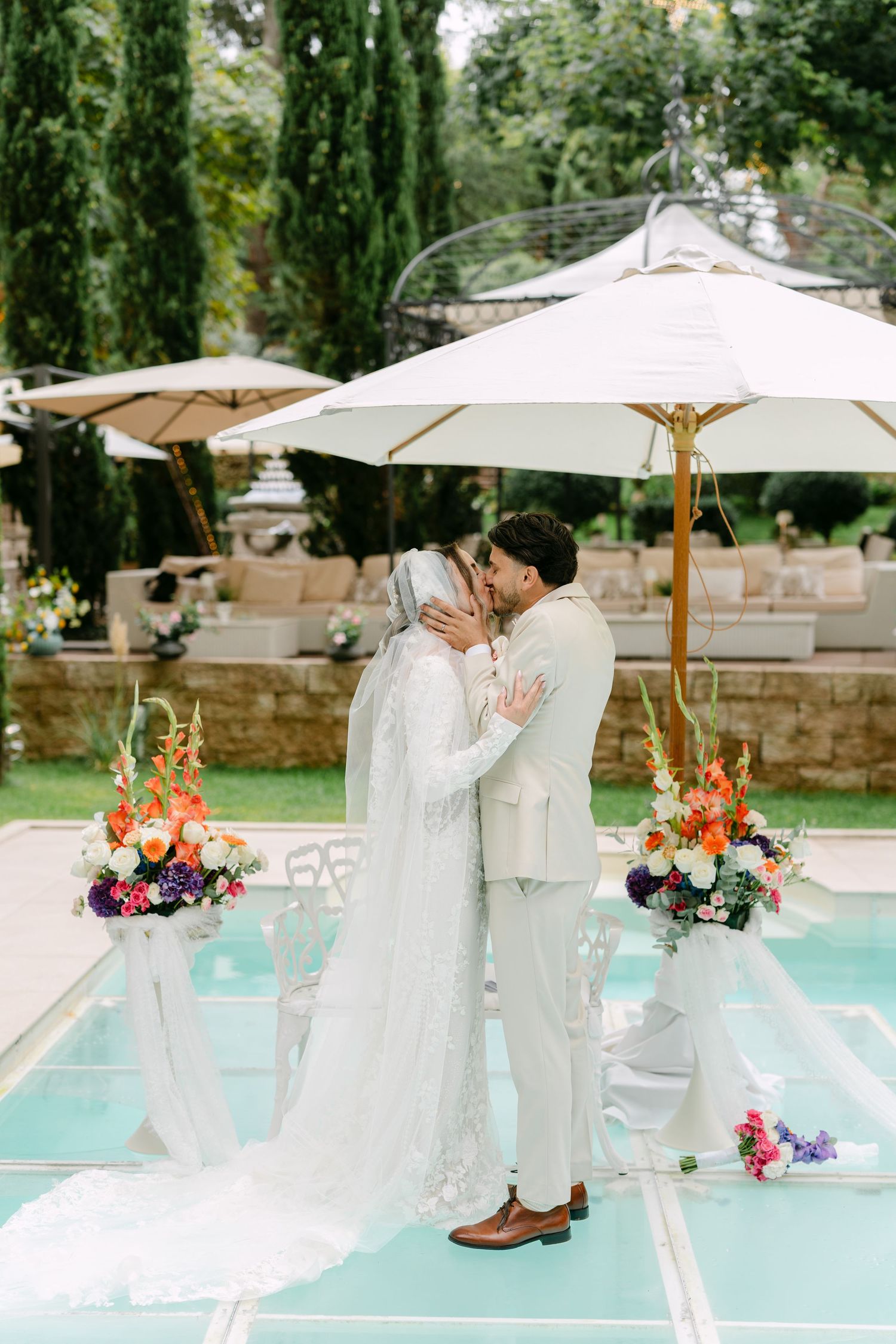 Romantic wedding couple sharing intimate moment under white umbrellas by pool.