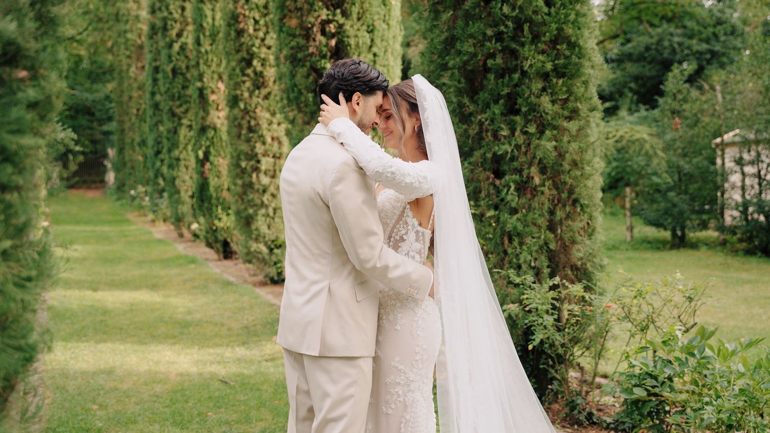 Wedding couple embraces in a lush garden setting surrounded by greenery and natural light.
