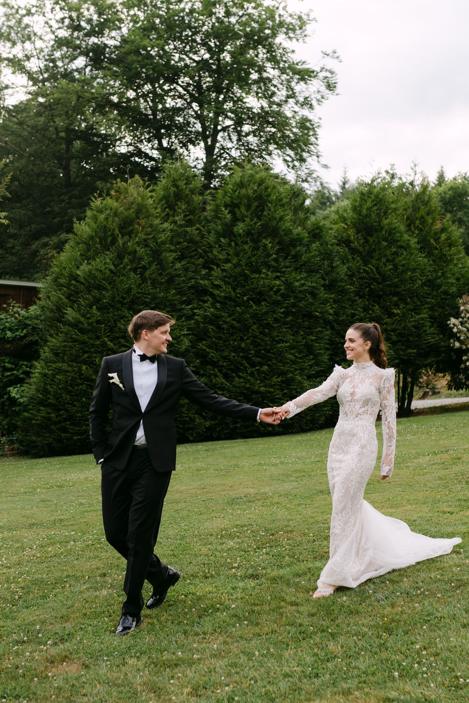 Couple performs playful dance moves on a green lawn during their wedding photoshoot.