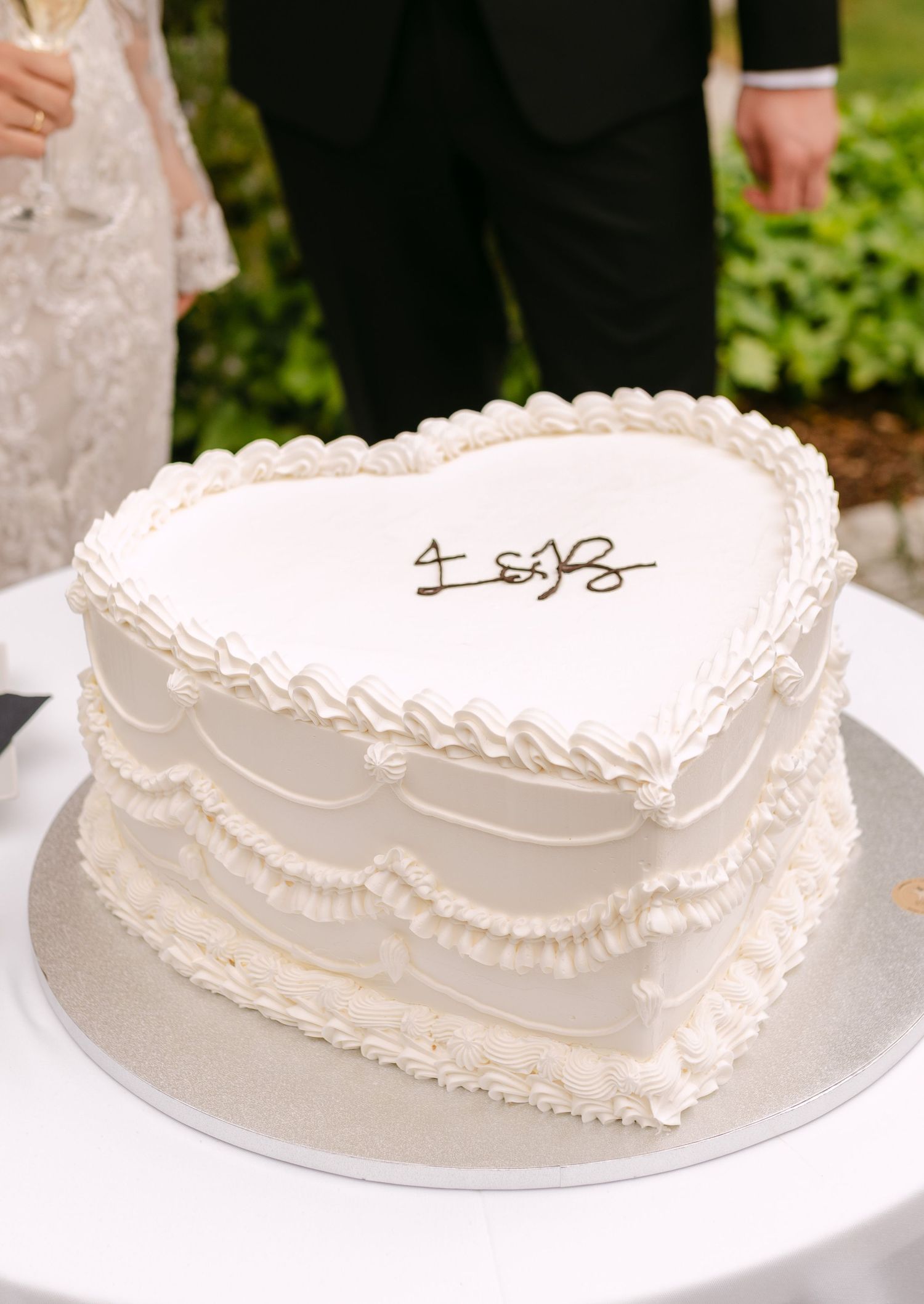 Heart-shaped white wedding cake with delicate piped frosting details displayed on a plate.
