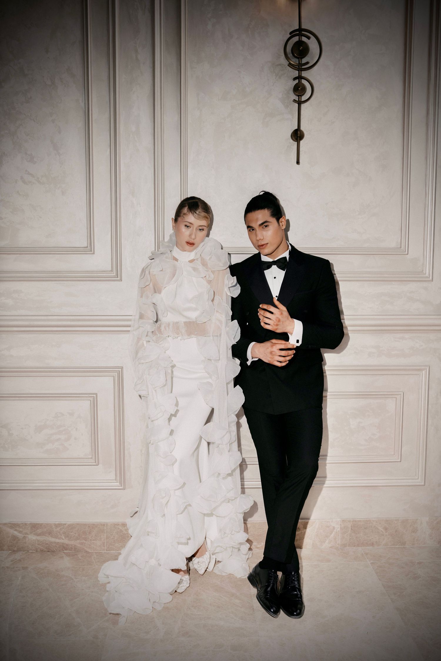 Artistic wedding photoshoot with couple sitting against elegant paneled wall.