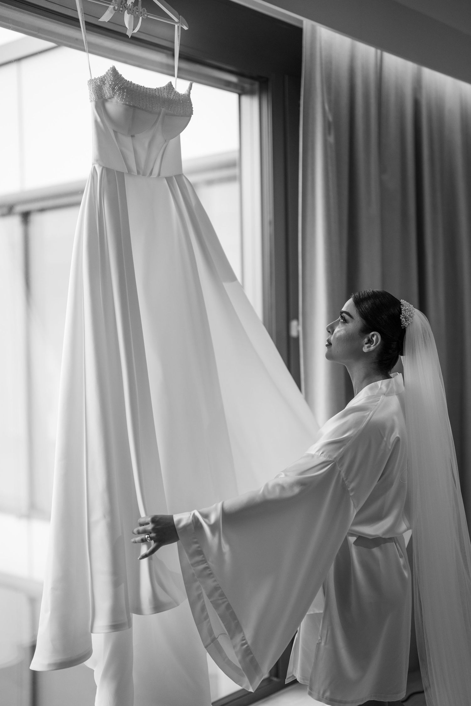 White wedding dresses and robes hanging in a bright, sunlit room during wedding preparations.