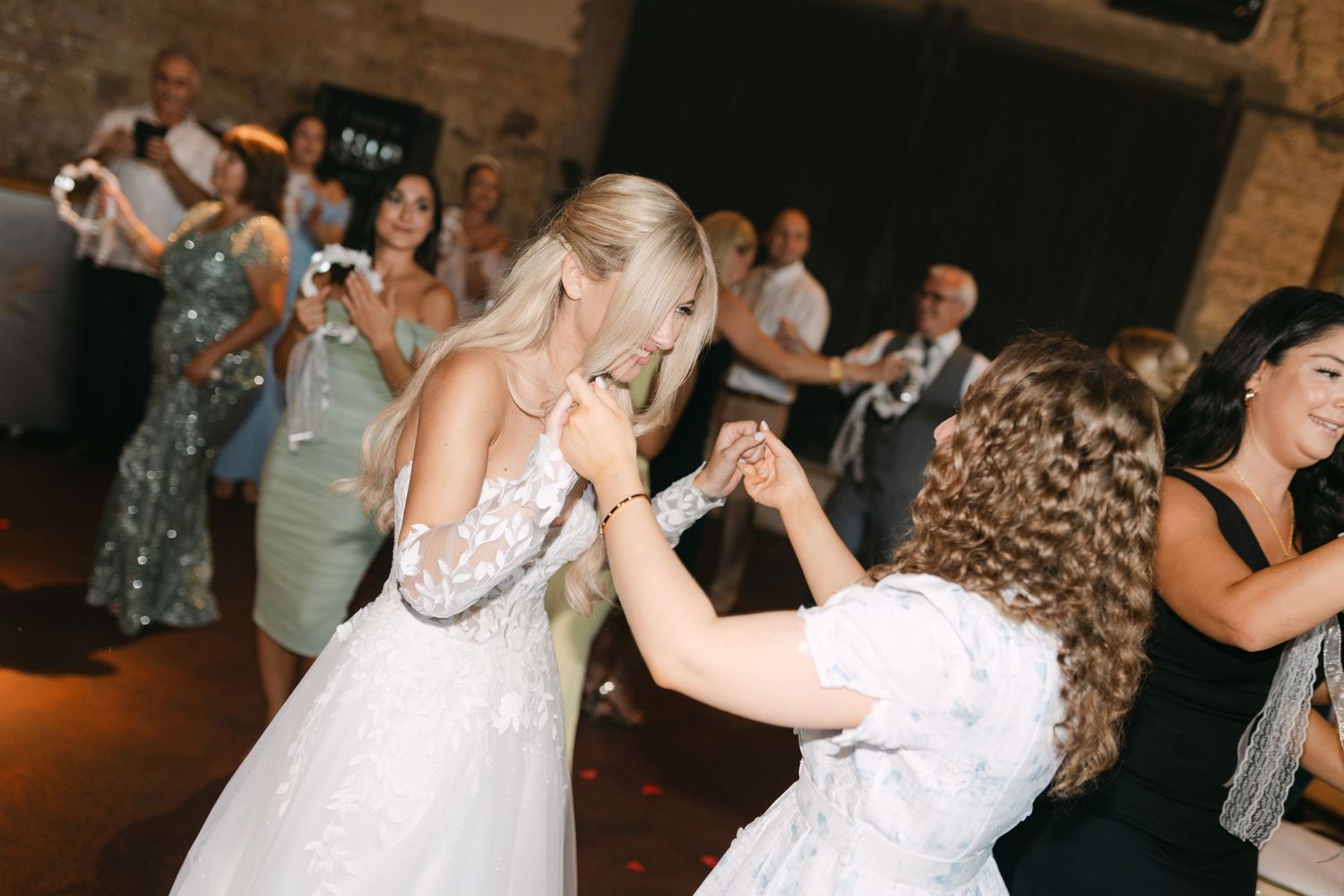 Wedding party dancing and celebrating in a rustic indoor venue with brick walls.