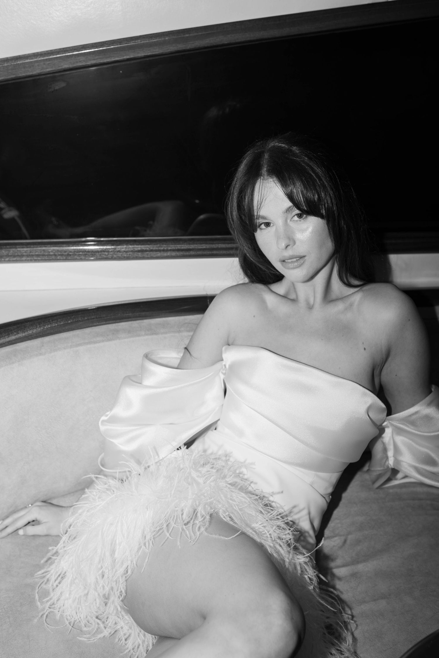 Black and white portrait of model wearing feathered white dress on couch.