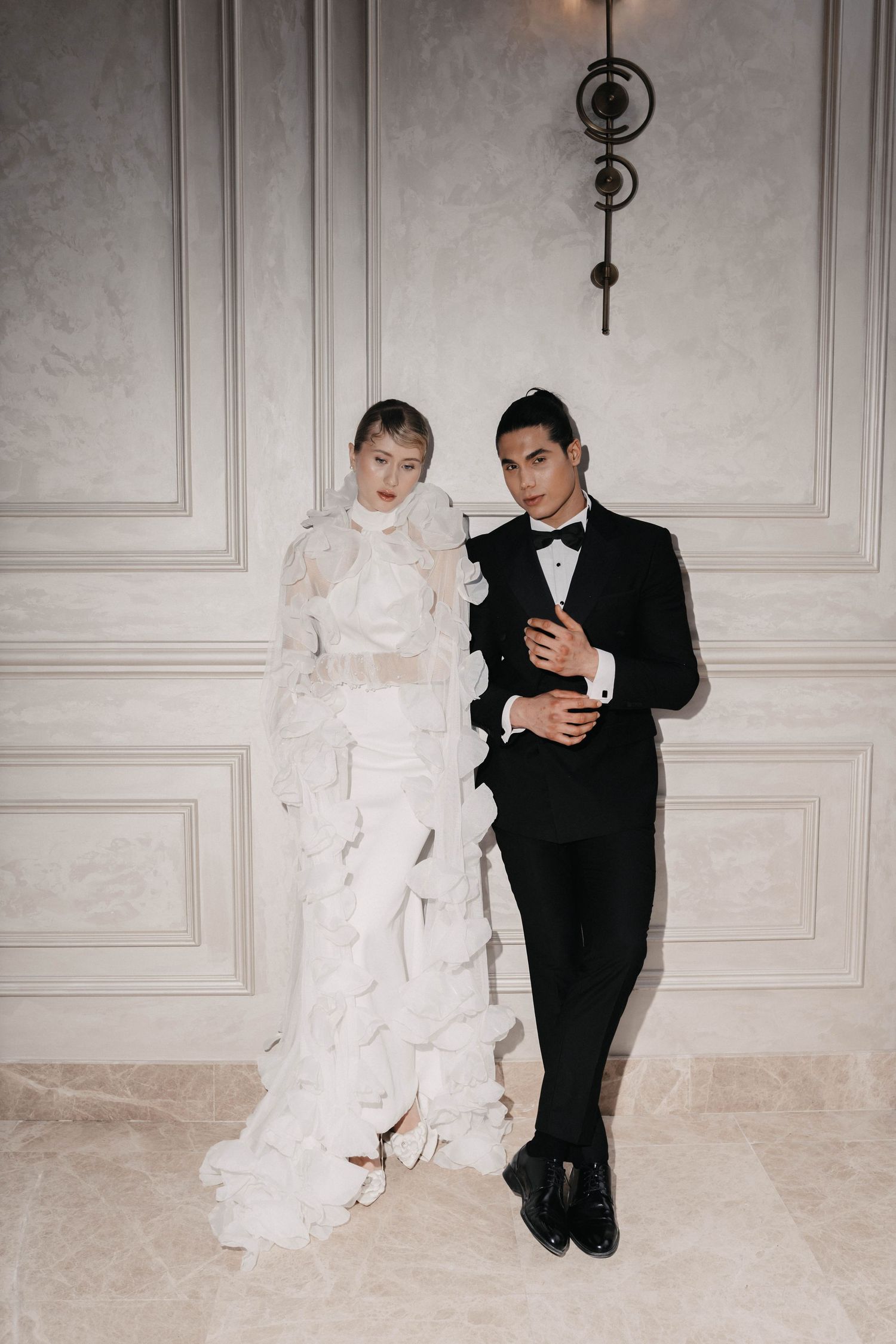 A couple poses together at a formal event, with one in an elegant white gown and the other in a classic black tuxedo.