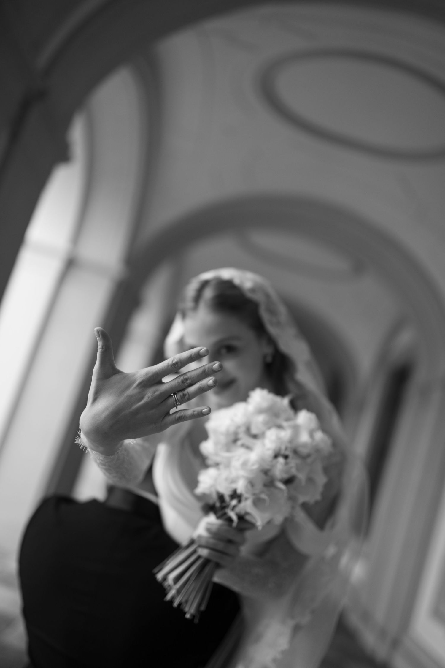 A black and white wedding photograph showing a bride holding a white floral bouquet with her hand raised in an elegant gesture.