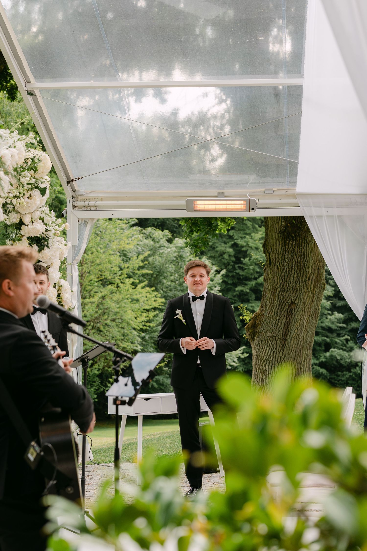 Formal ceremony under white tent canopy with greenery and floral decorations.