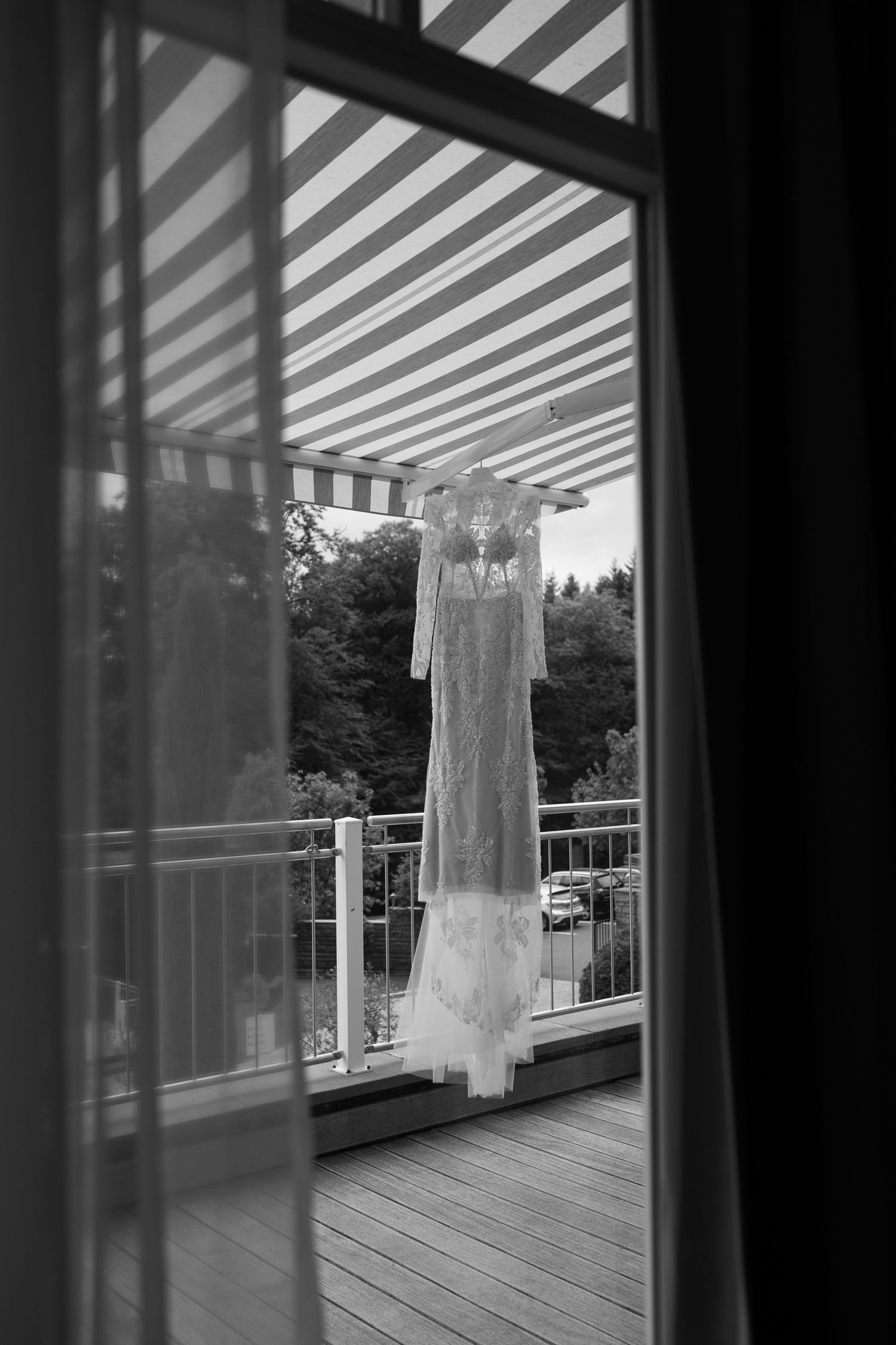 White dress hanging on a balcony with striped shadows from pergola overhead.